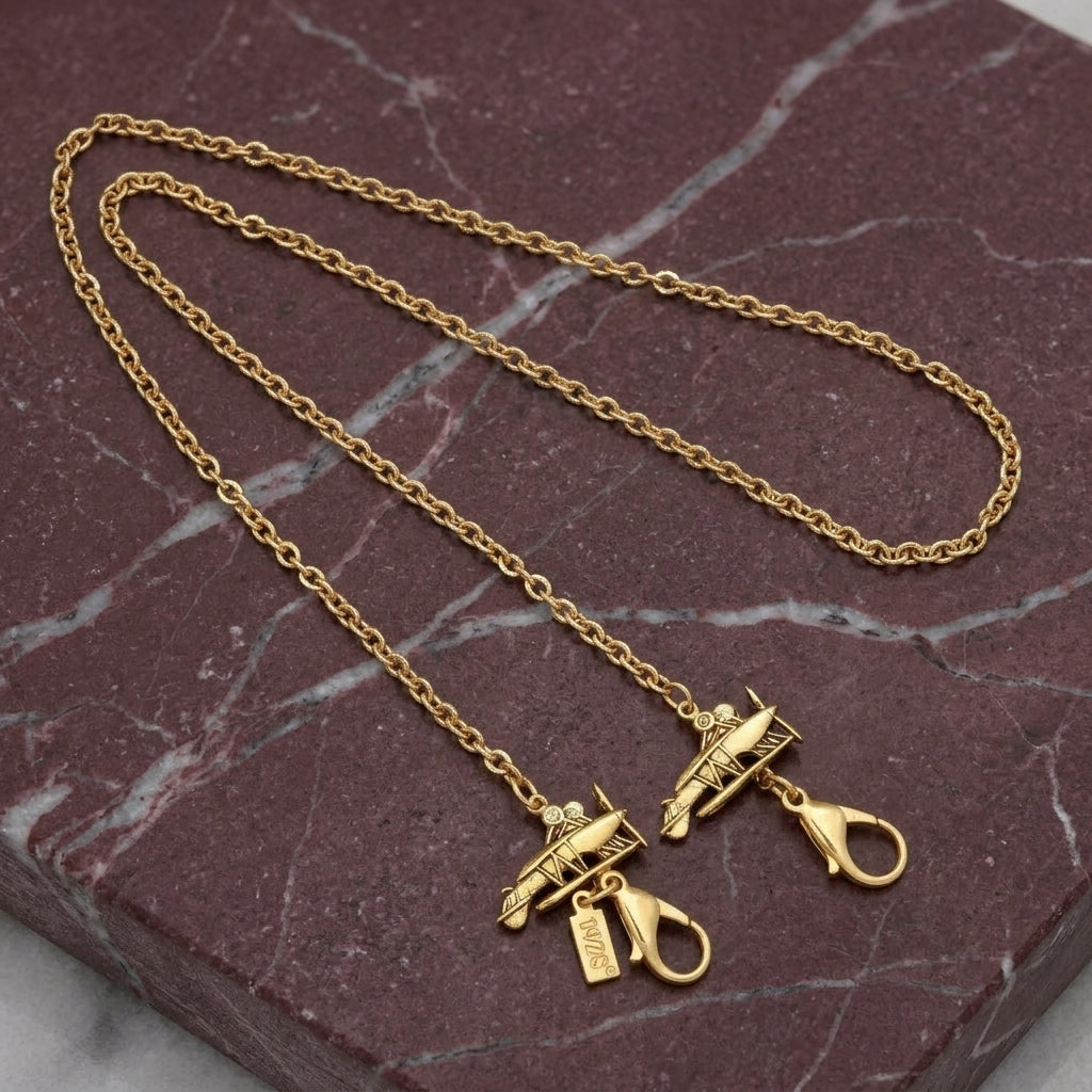 Gold tone Airplane Face Mask Chain Holder resting on muted red marble stone