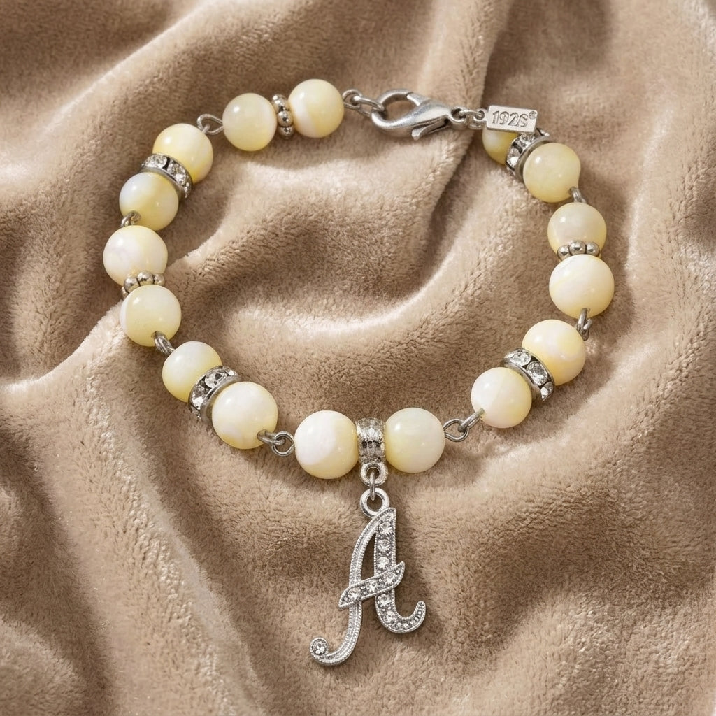Mother Of Pearl Crystal Initial Charm Bracelet resting on light-colored fabric