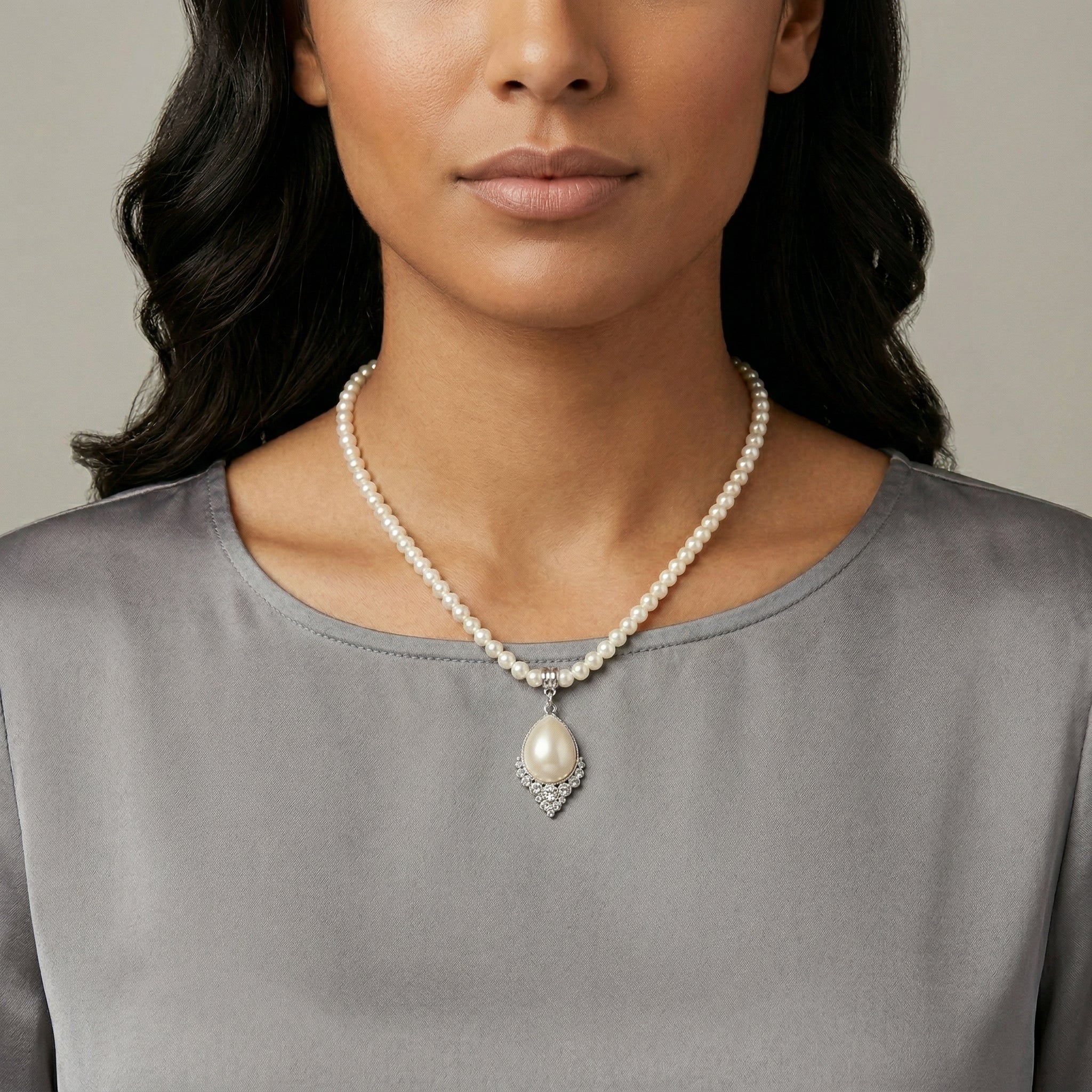 Woman wearing a pearl necklace with a gray top against a neutral background