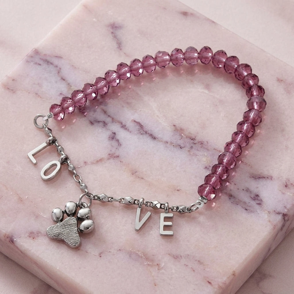 Pink beaded bracelet with paw charm and 'LOVE' letters on a marble surface