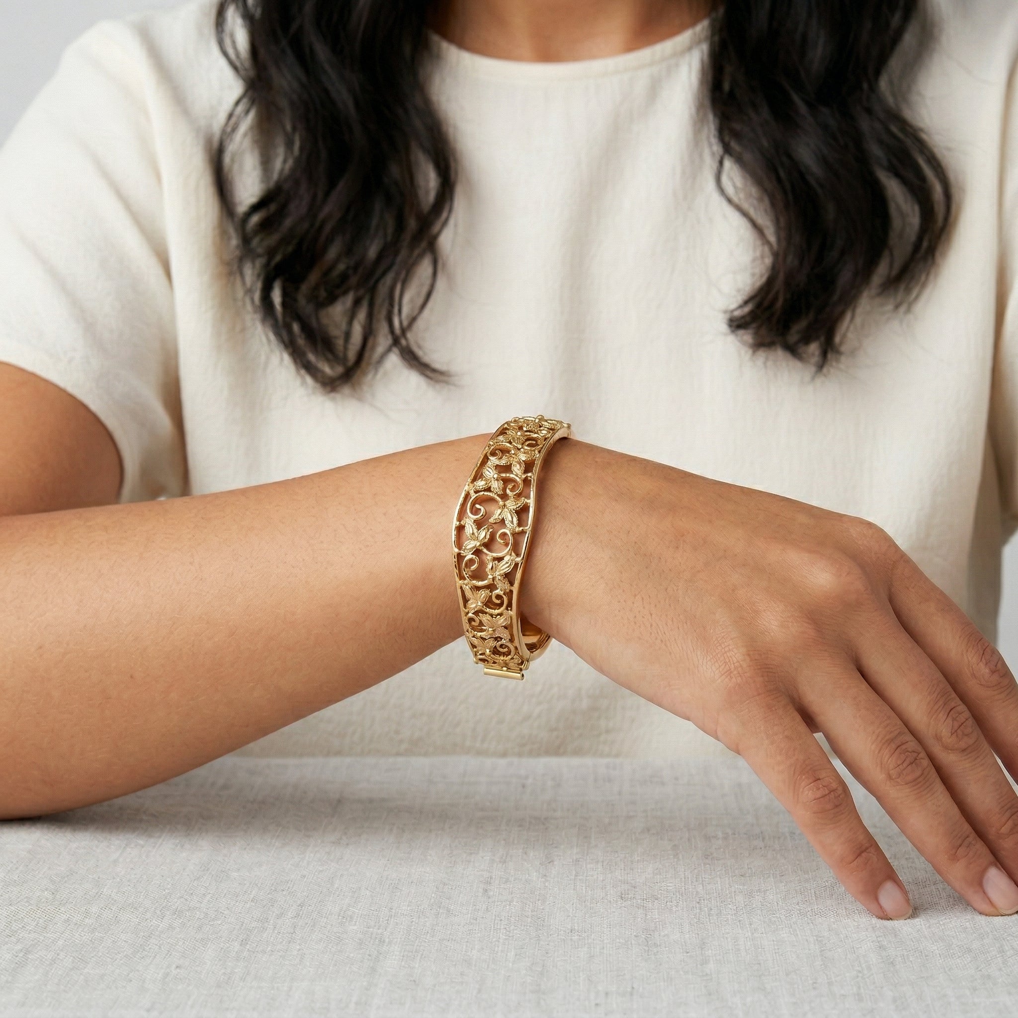 Woman in a white outfit showing a Gold Floral Hinge Bracelet on her wrist