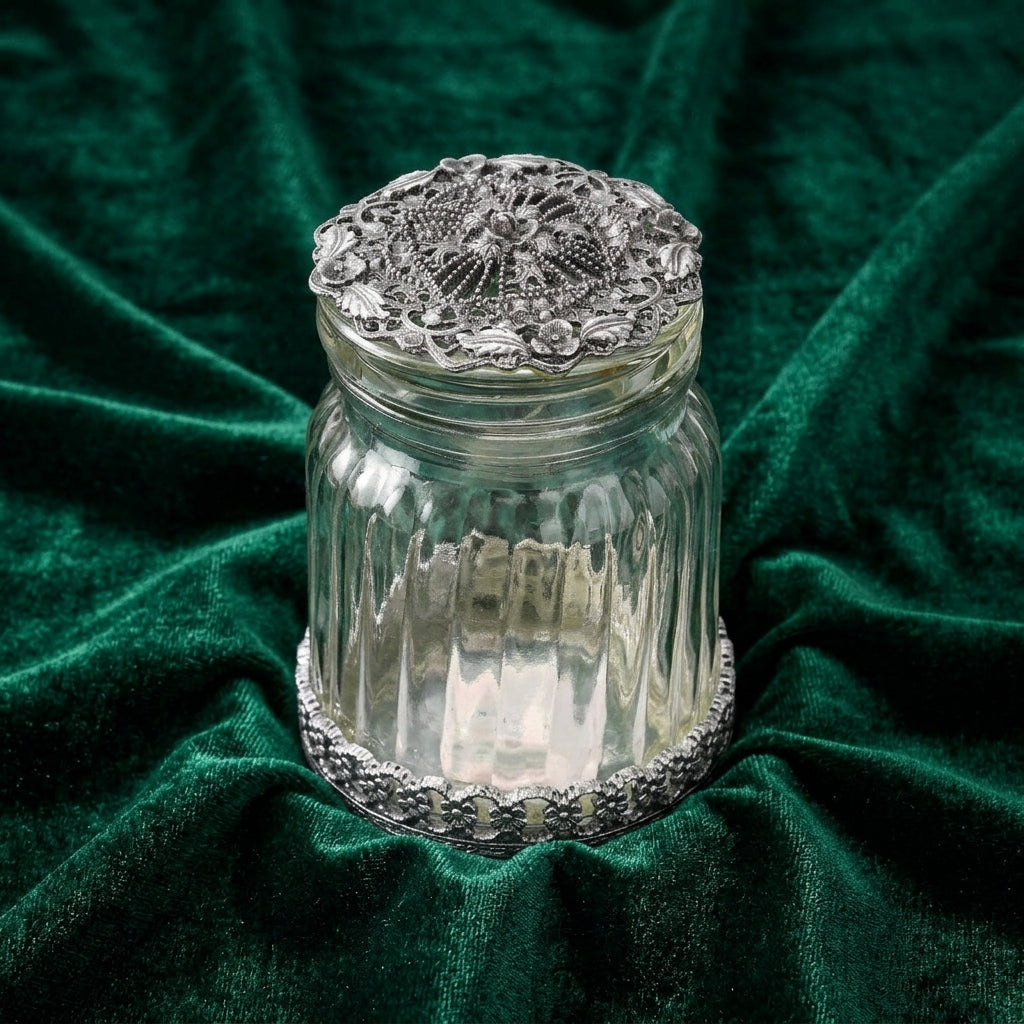 Decorative glass jar with a silver lid on a green fabric background