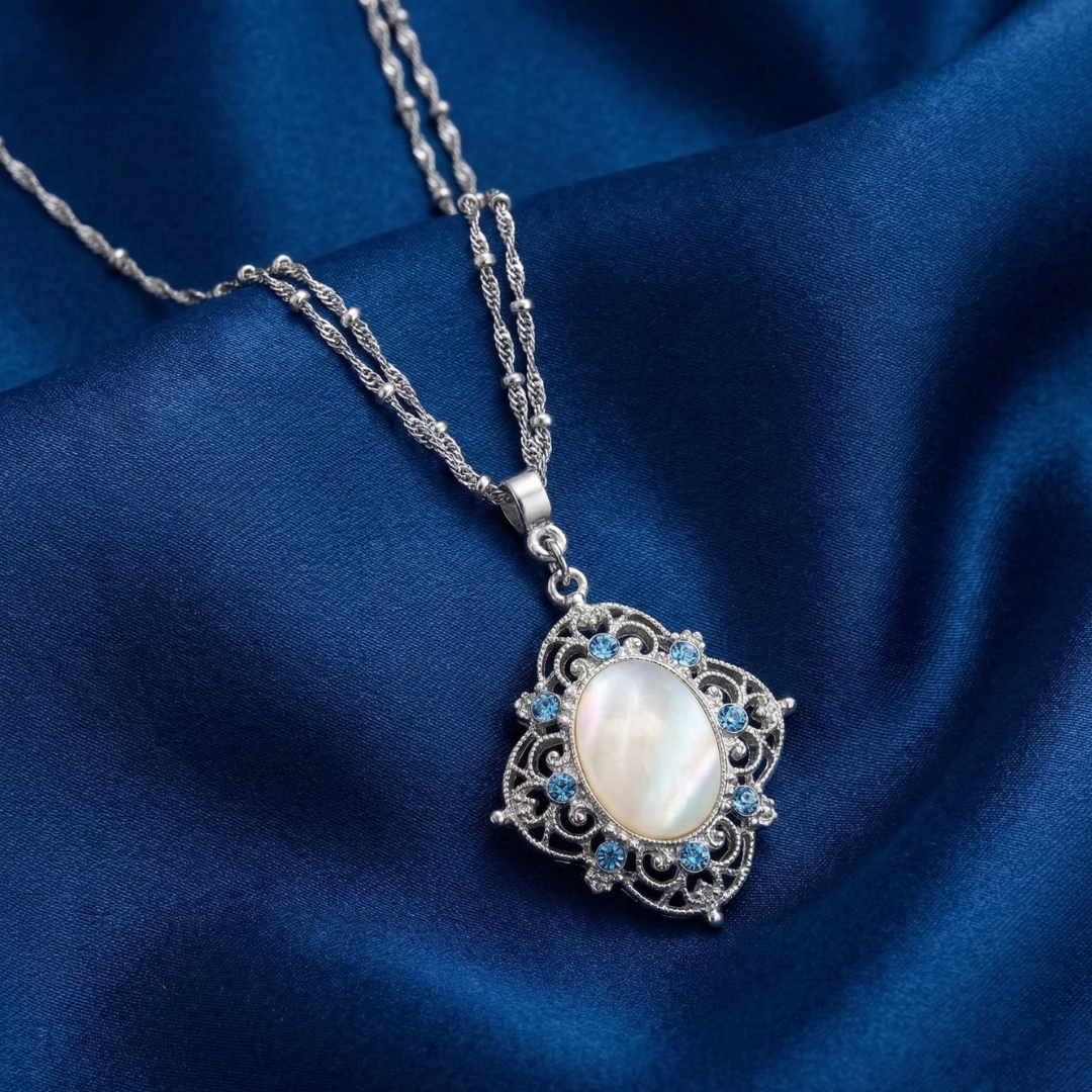 Silver necklace with a pendant featuring an ivory gemstone and small blue crystals on a blue fabric background