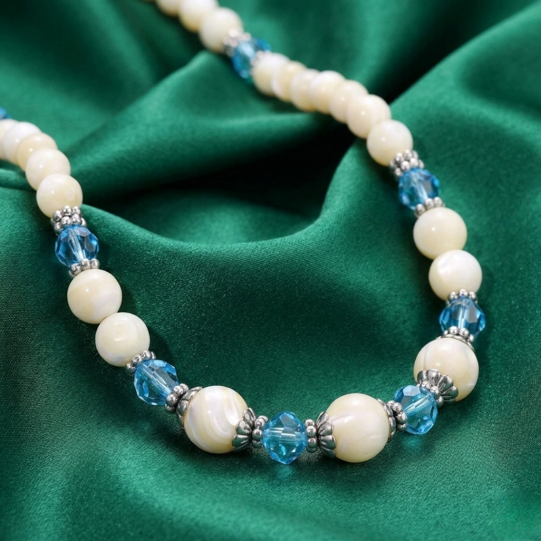 Necklace with white faux pearls and blue beads on a green fabric background