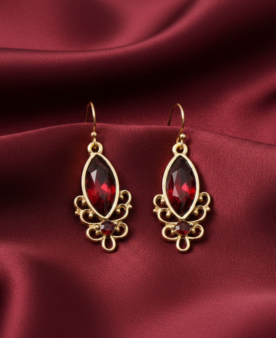 Gold earrings with red gemstones on a maroon fabric background