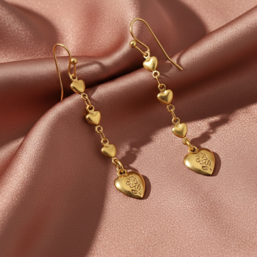 Gold heart-shaped earrings on a pink fabric background