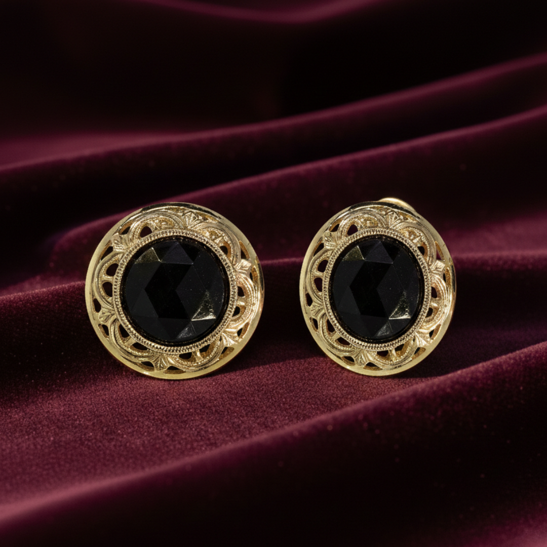 Gold earrings with black gemstones on a maroon fabric background