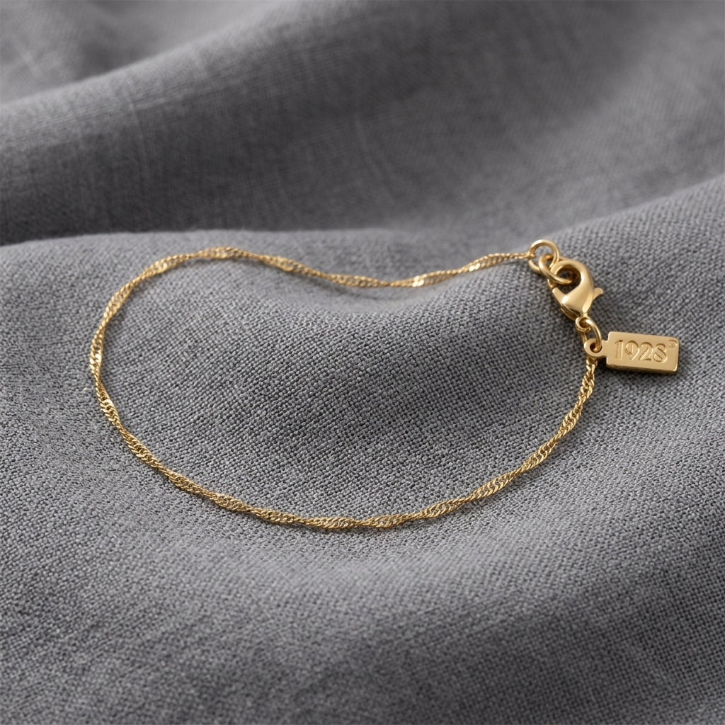 A delicate gold chain bracelet with a lobster clasp displayed on a textured gray fabric background.