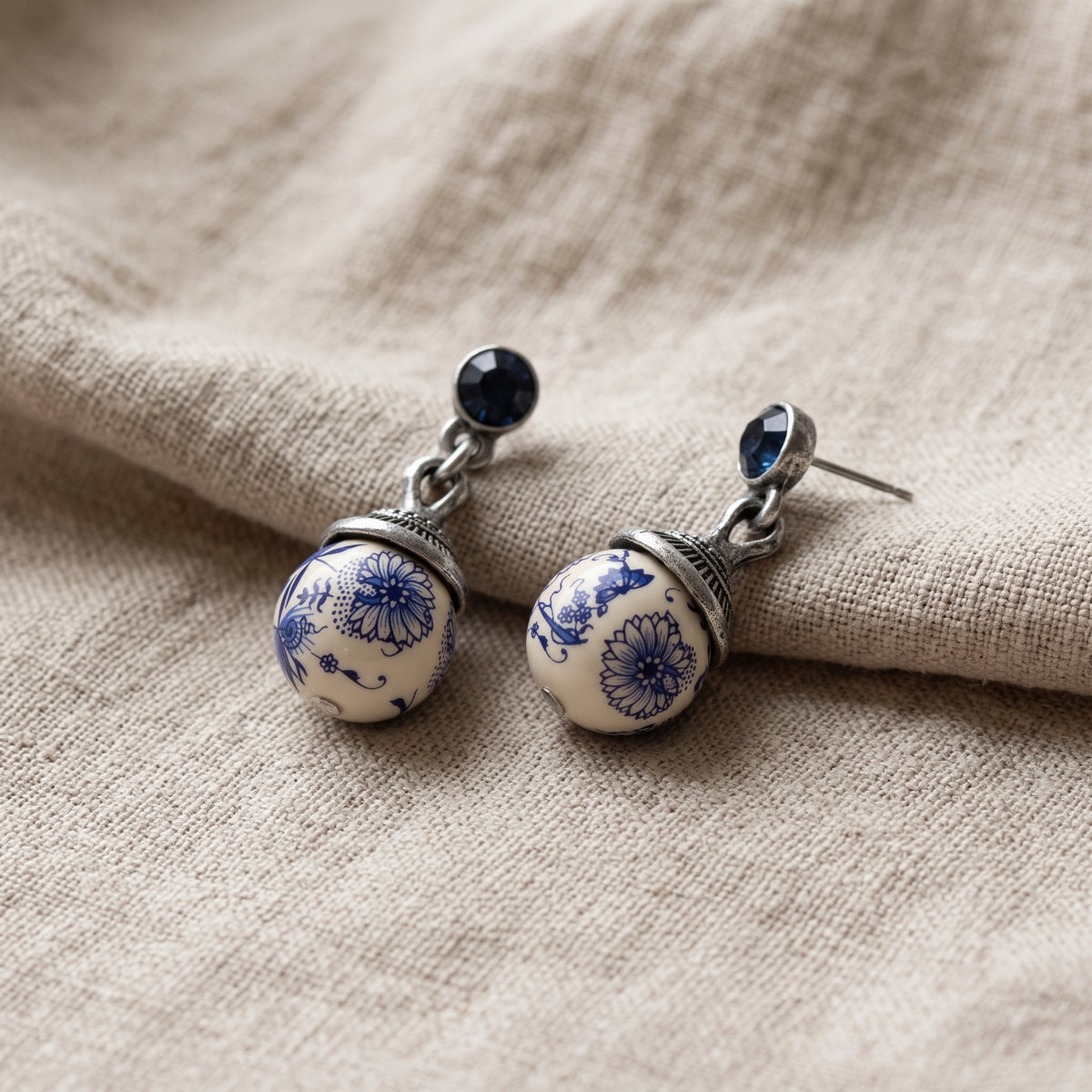Blue Willow Round Beaded Post Drop Earrings resting on a beige linen fabric surface