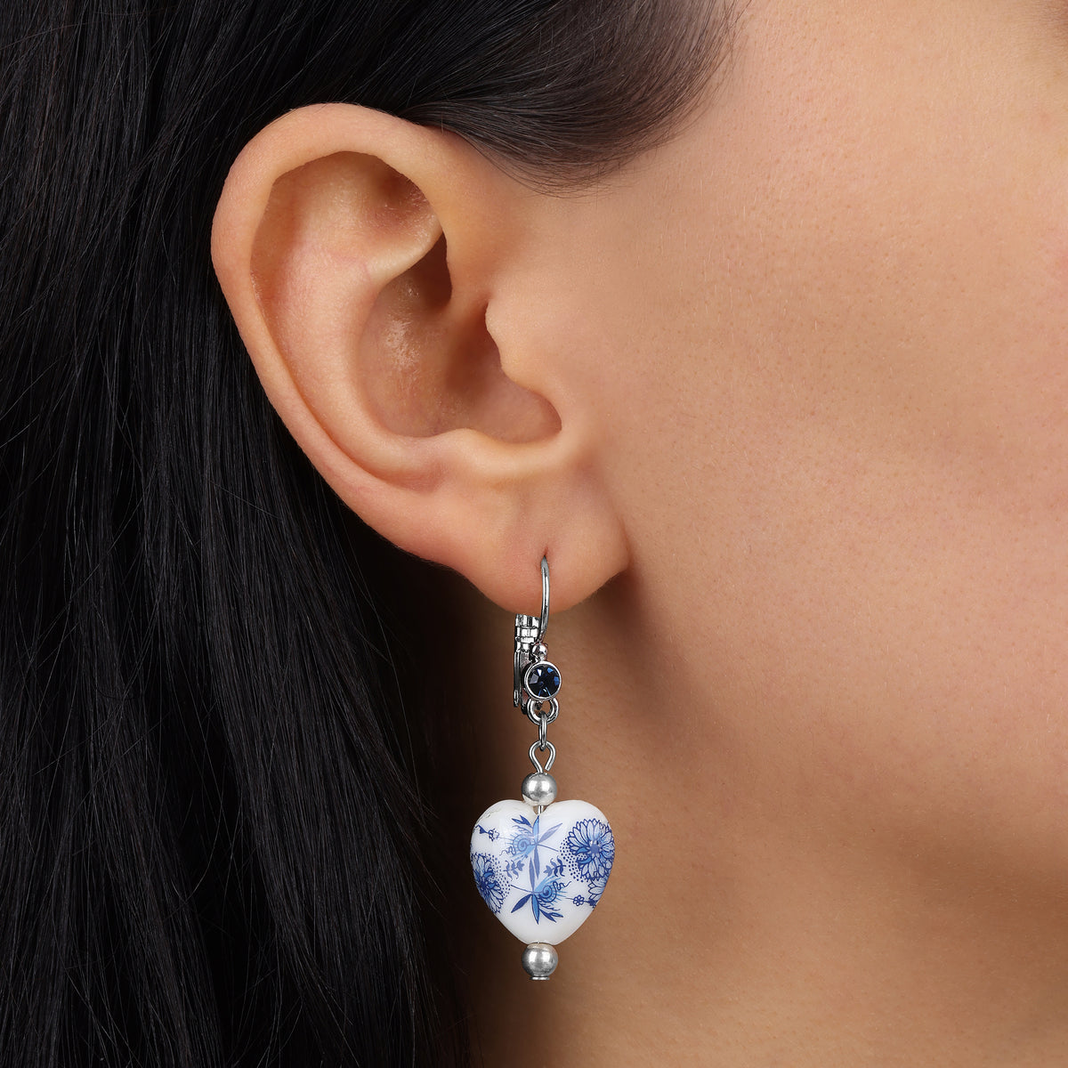 A close-up of a person's ear wearing a Blue Willow Blue Stone Heart Drop Earrings