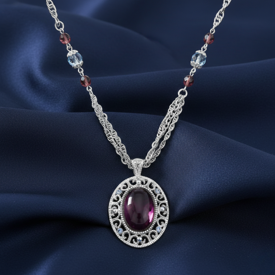 Silver necklace with a purple crystal pendant and several crystals on the chain and outline of the pendant on a dark blue fabric background