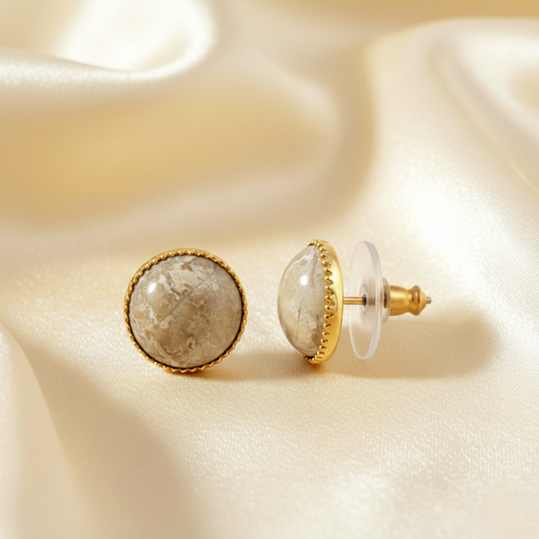 Pair of earrings with gold and stone design on a beige fabric background