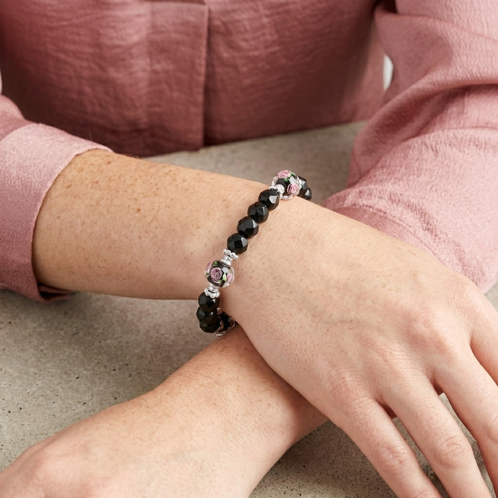 Woman in a soft pink shirt wearing a black beaded bracelet with pink floral designs on her wrist
