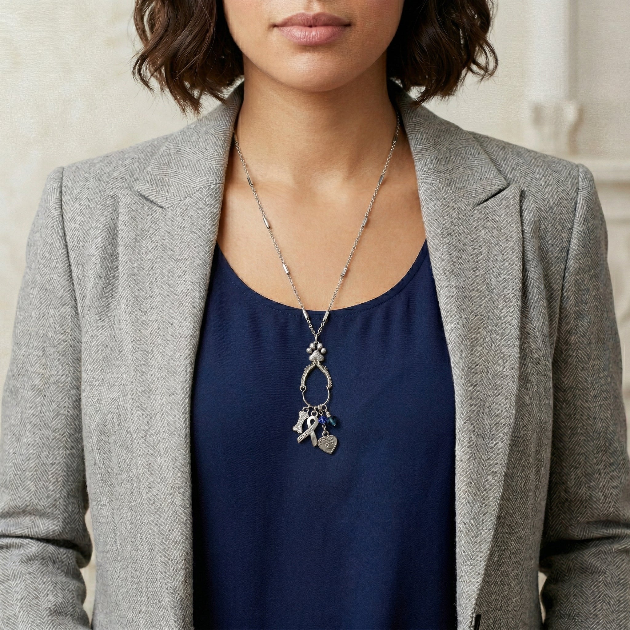 Woman in a gray blazer and a blue shirt wearing a silver tone charm necklace that as four distinct pet rescue-inspired charms