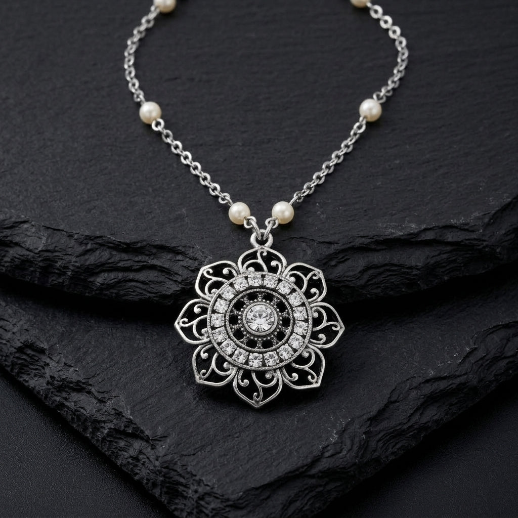 Silver tone floral pendant necklace that has clear crystal accents and white faux pearls on the chain resting on black stone surface