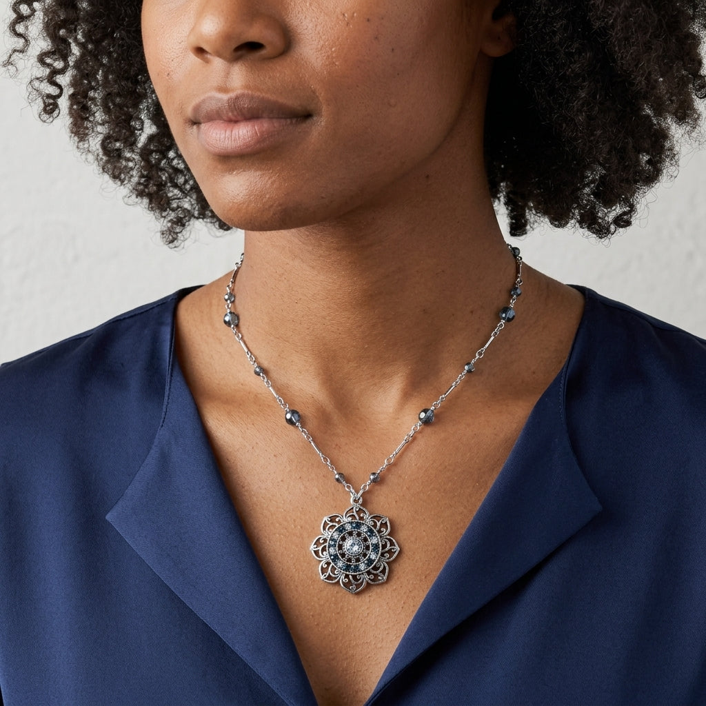 Woman wearing a blue blouse with a silver tone floral pendant necklace that has blue beads and crystals