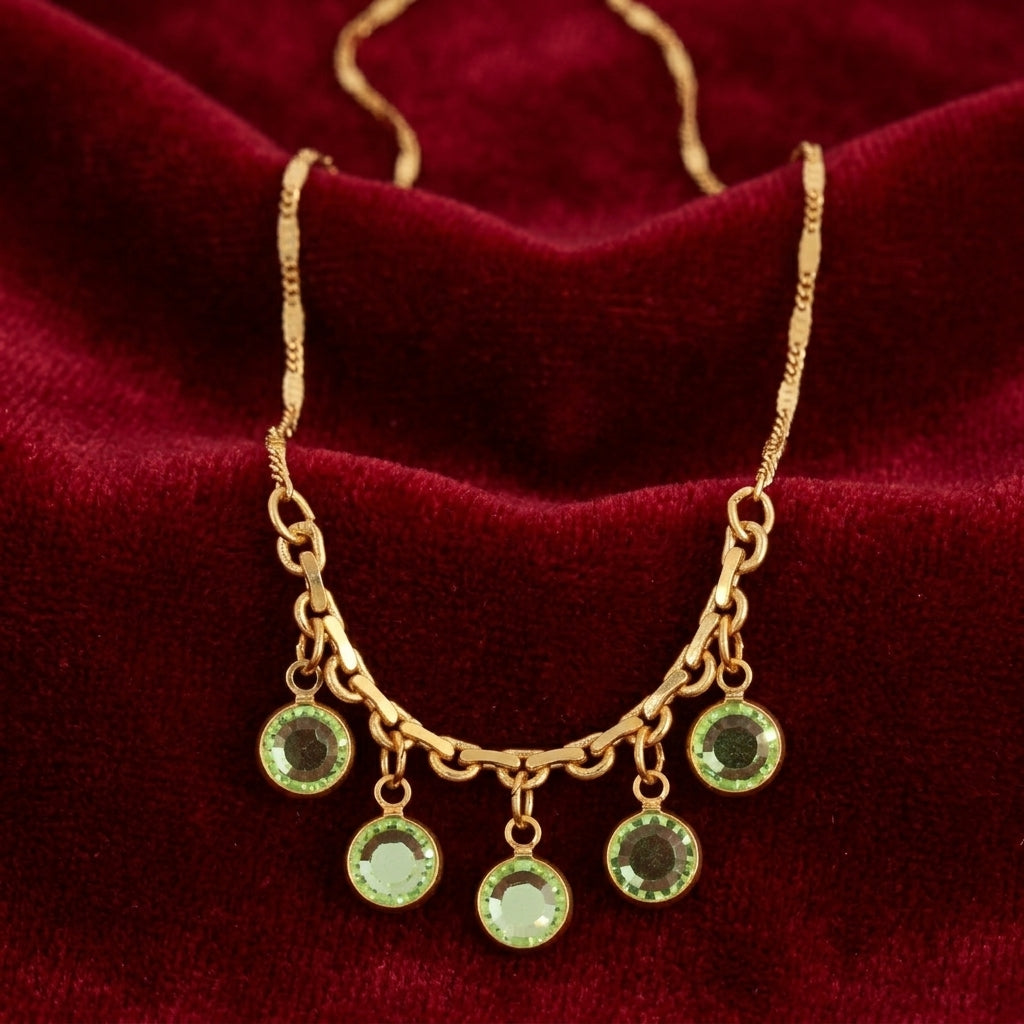 Gold tone necklace that has dangling green Austrian channel crystals resting on red fabric