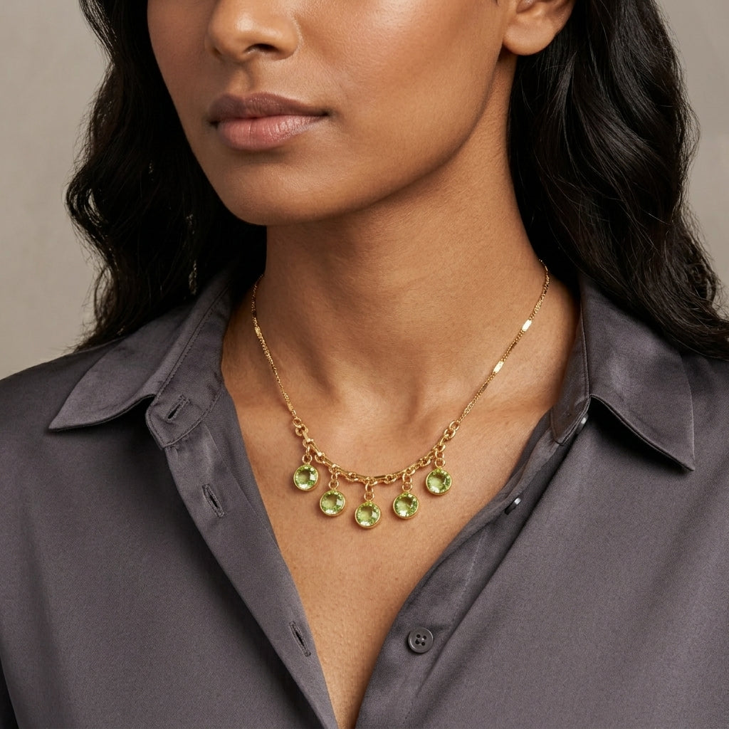 Woman in a dark blouse wearing a gold tone necklace that has dangling green Austrian channel crystals