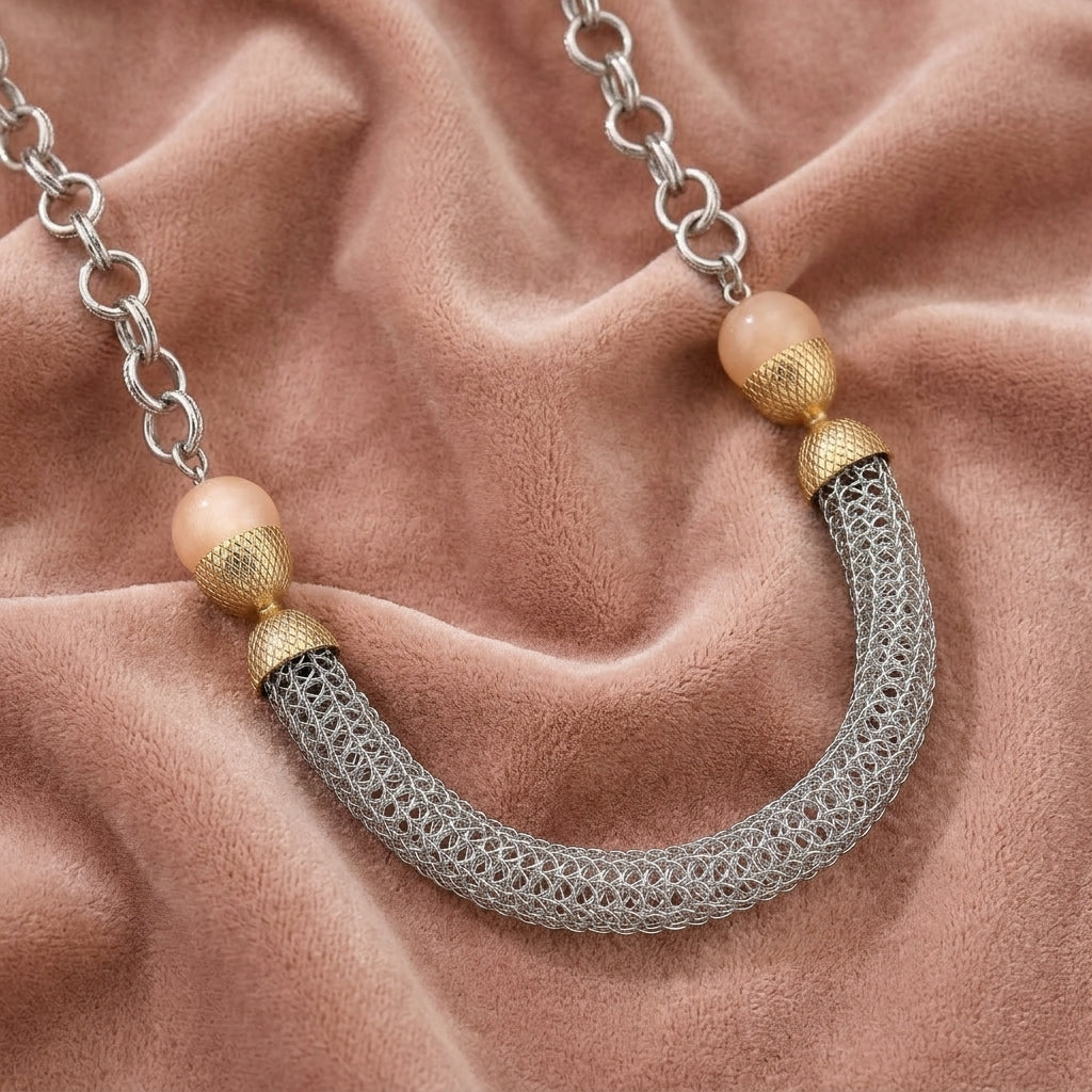 Beige moonstone necklace that has silver tone tube and mesh chains resting on light pink fabric