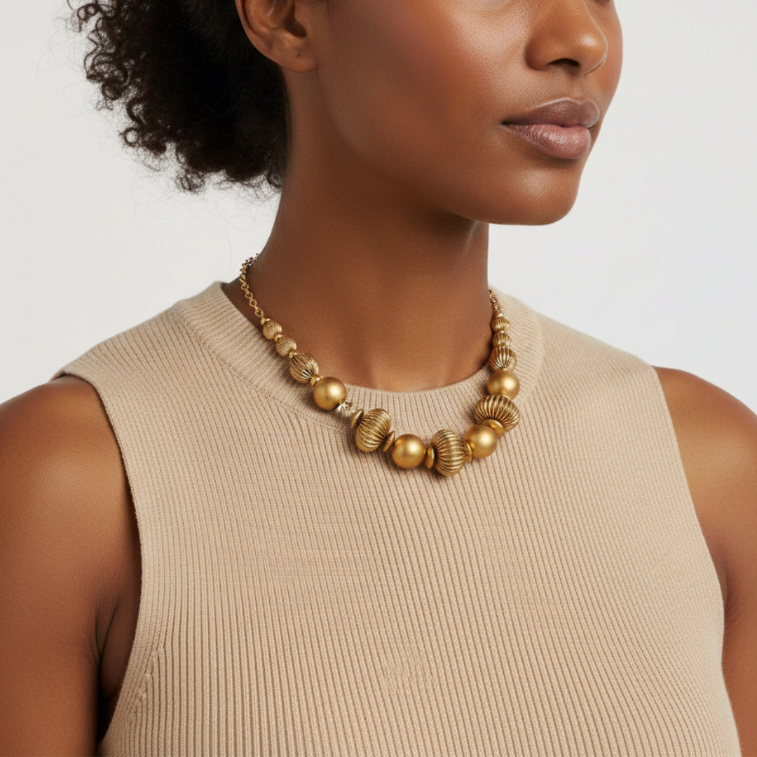 Woman wearing a gold tone beaded necklace against a neutral background