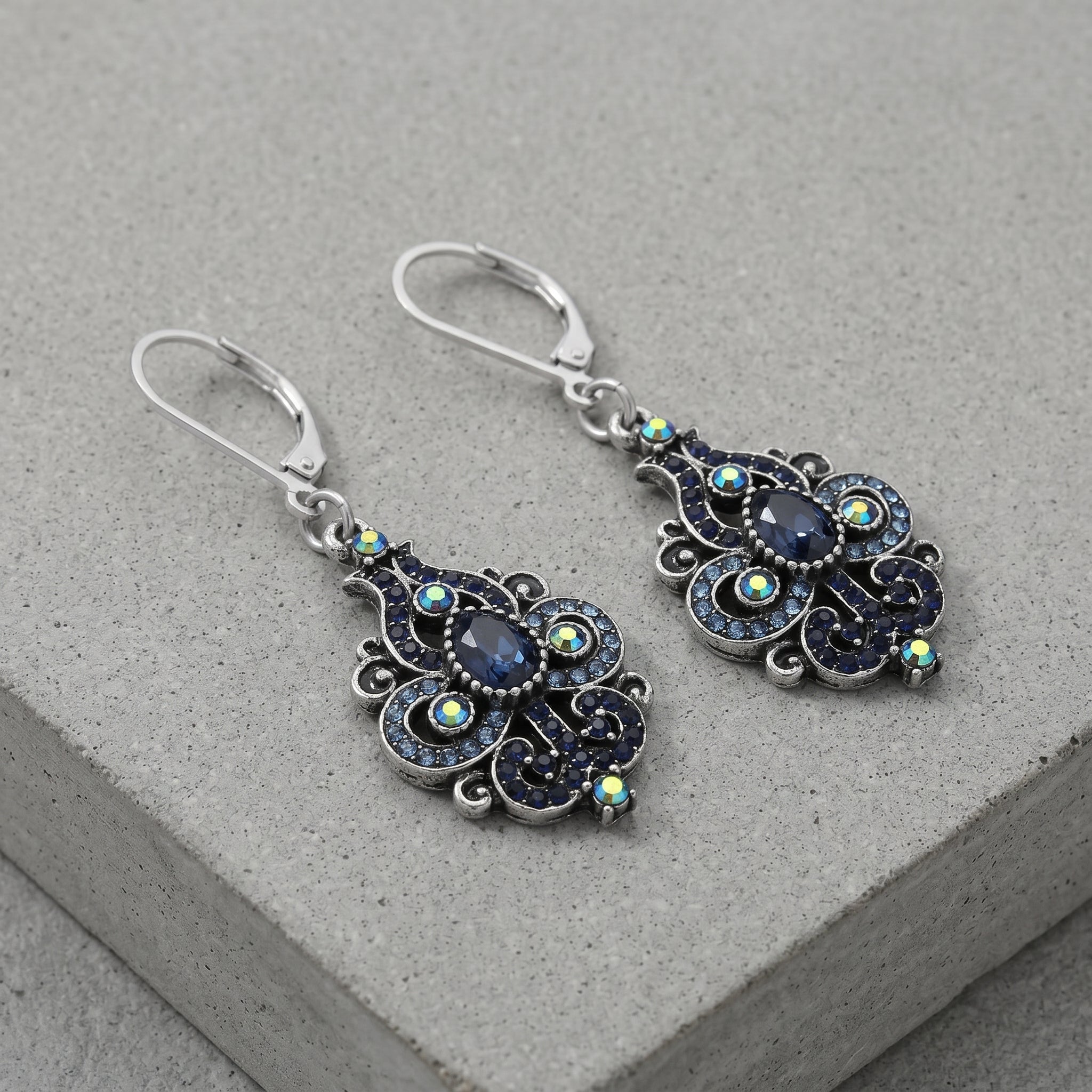 Giovane Iridescent AB Crystal & Blue Stone Spade Drop Earrings on a gray stone surface