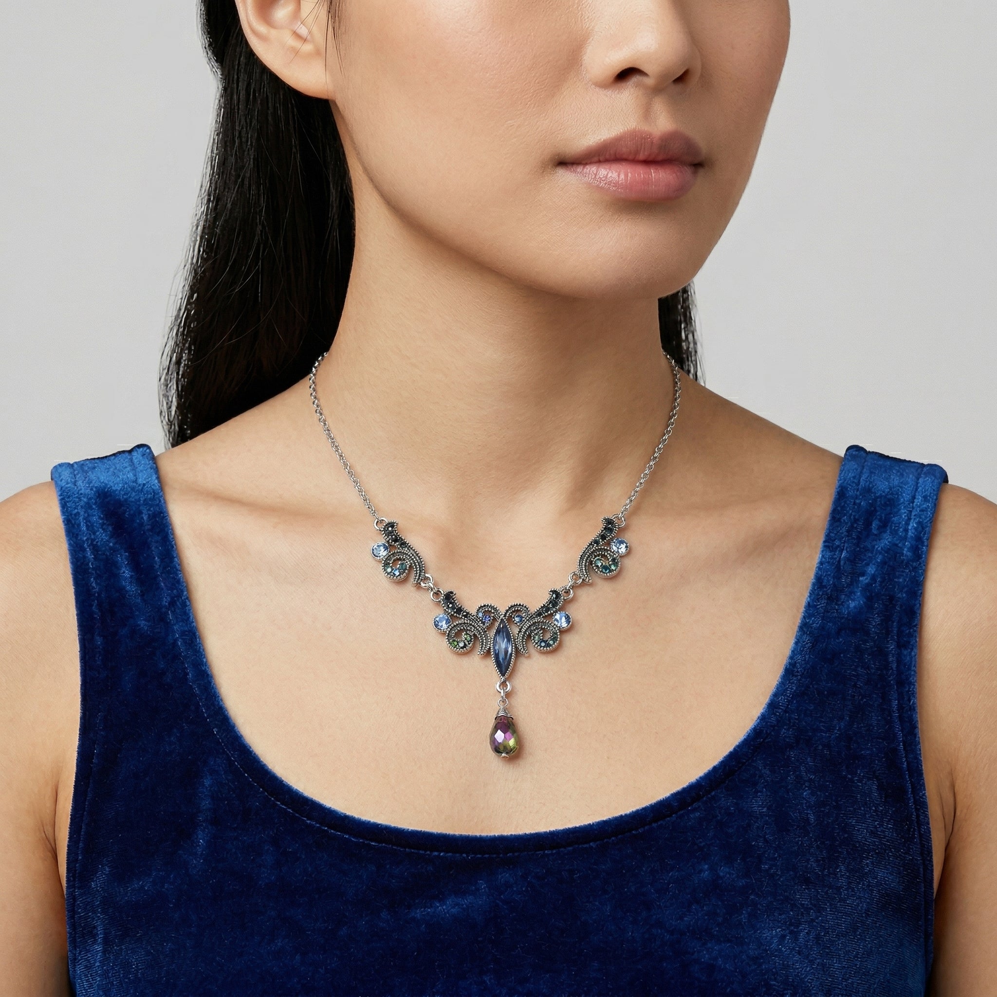Woman wearing a detailed AB crystal necklace with a blue top against a neutral background