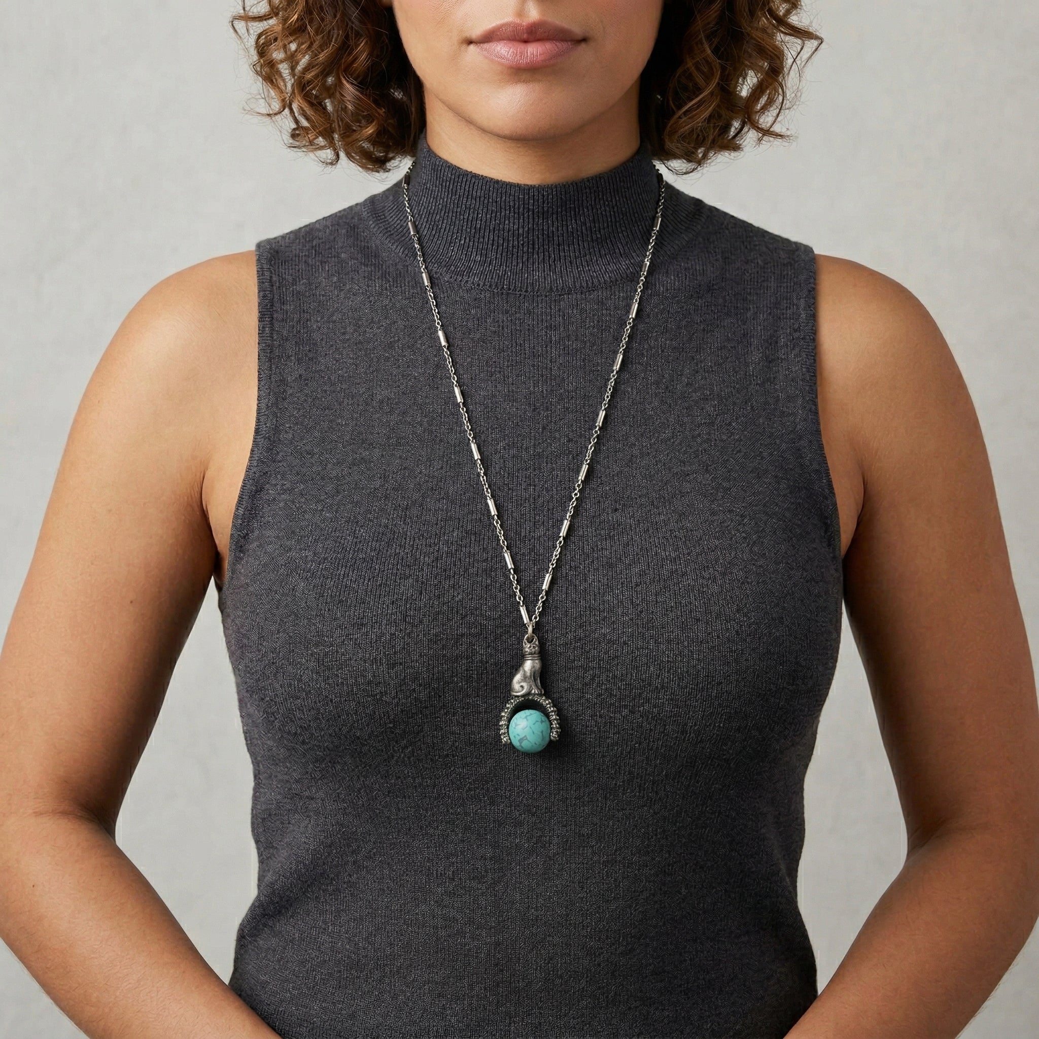 Woman in a dark gray sleeveless top wearing a silver tone tube chain cat and turquoise stone spinner pendant necklace