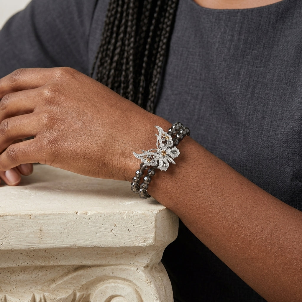 Person wearing a black beaded bracelet with a silver butterfly charm on an ornate surface