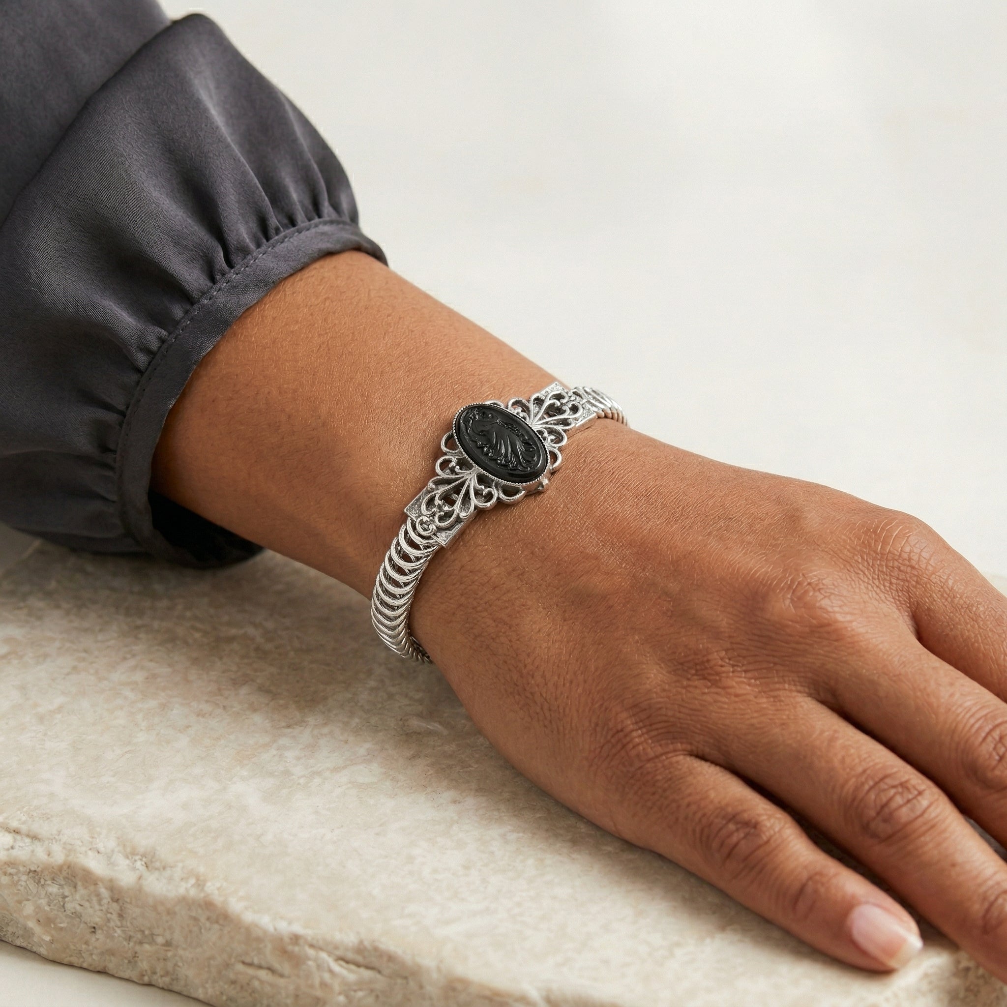Silver bracelet with a black stone on a wrist against a neutral background
