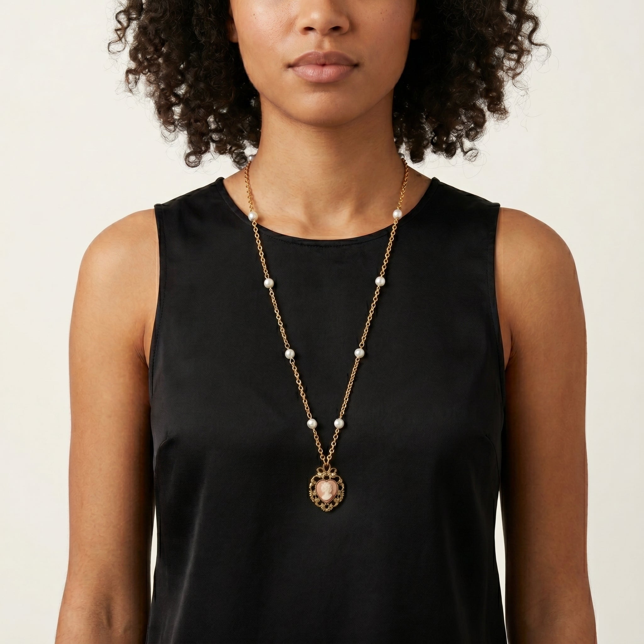Woman wearing a gold tone chain necklace with white faux pearls and a pink heart-shaped cameo pendant