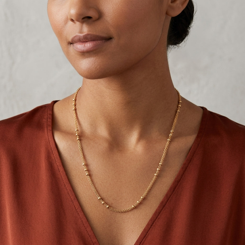 Woman wearing a gold tone necklace against a neutral background with a soft red-colored top