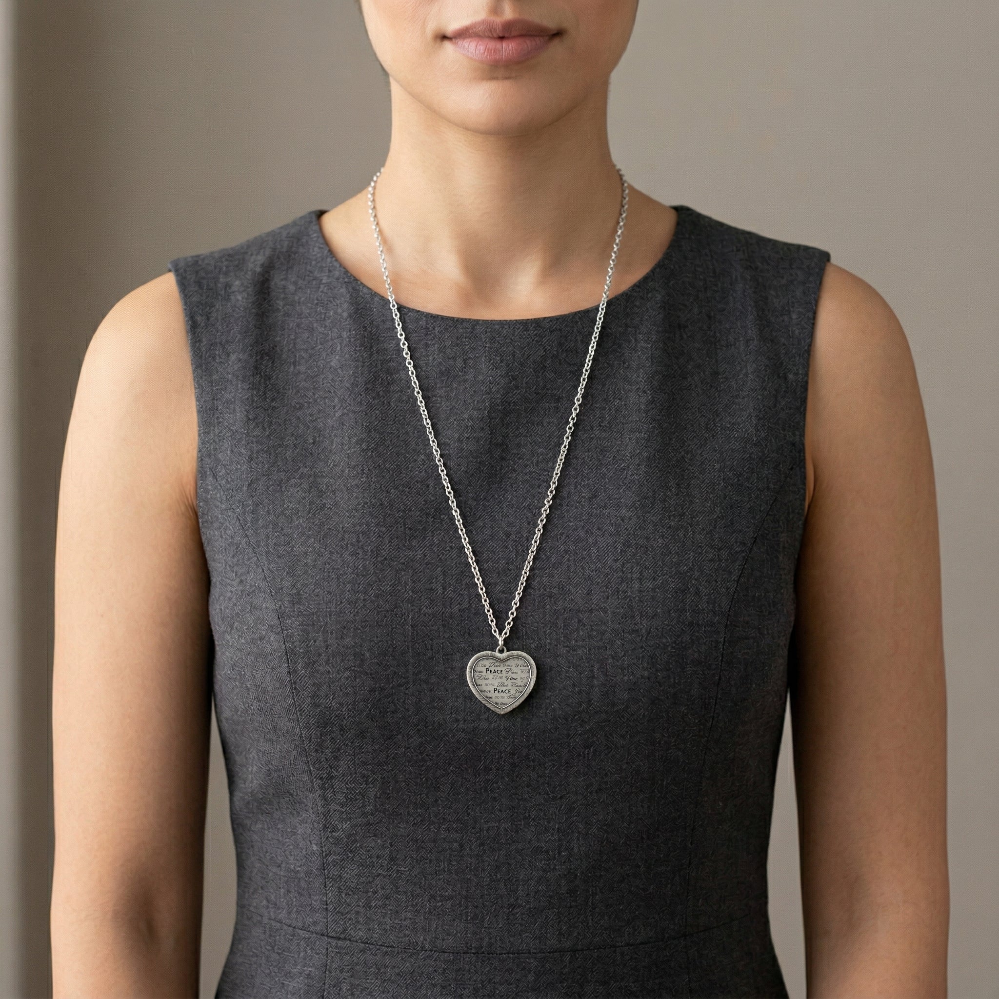 Woman wearing a dark gray sleeveless top with a silver necklace featuring a heart-shaped peace pendant.