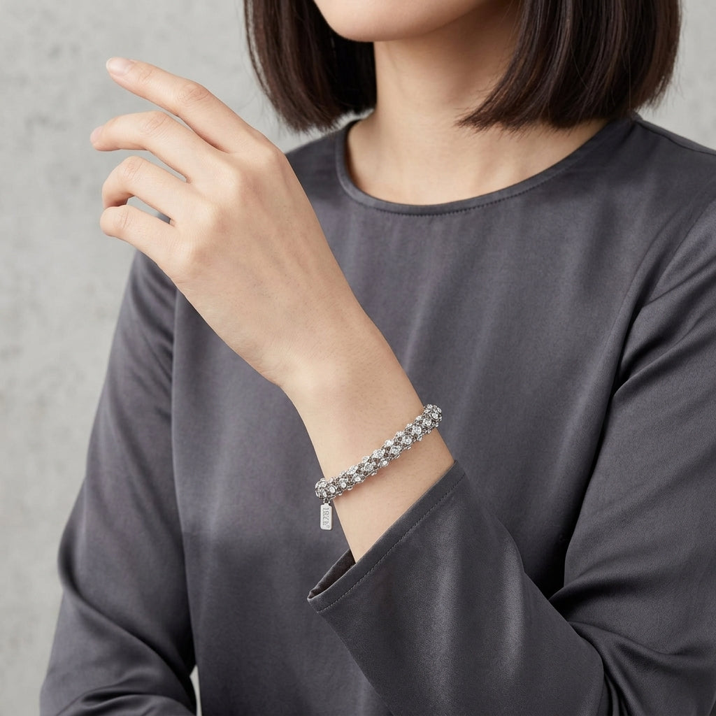 Person wearing a silver bracelet with shimmering clear crystals on a plain background