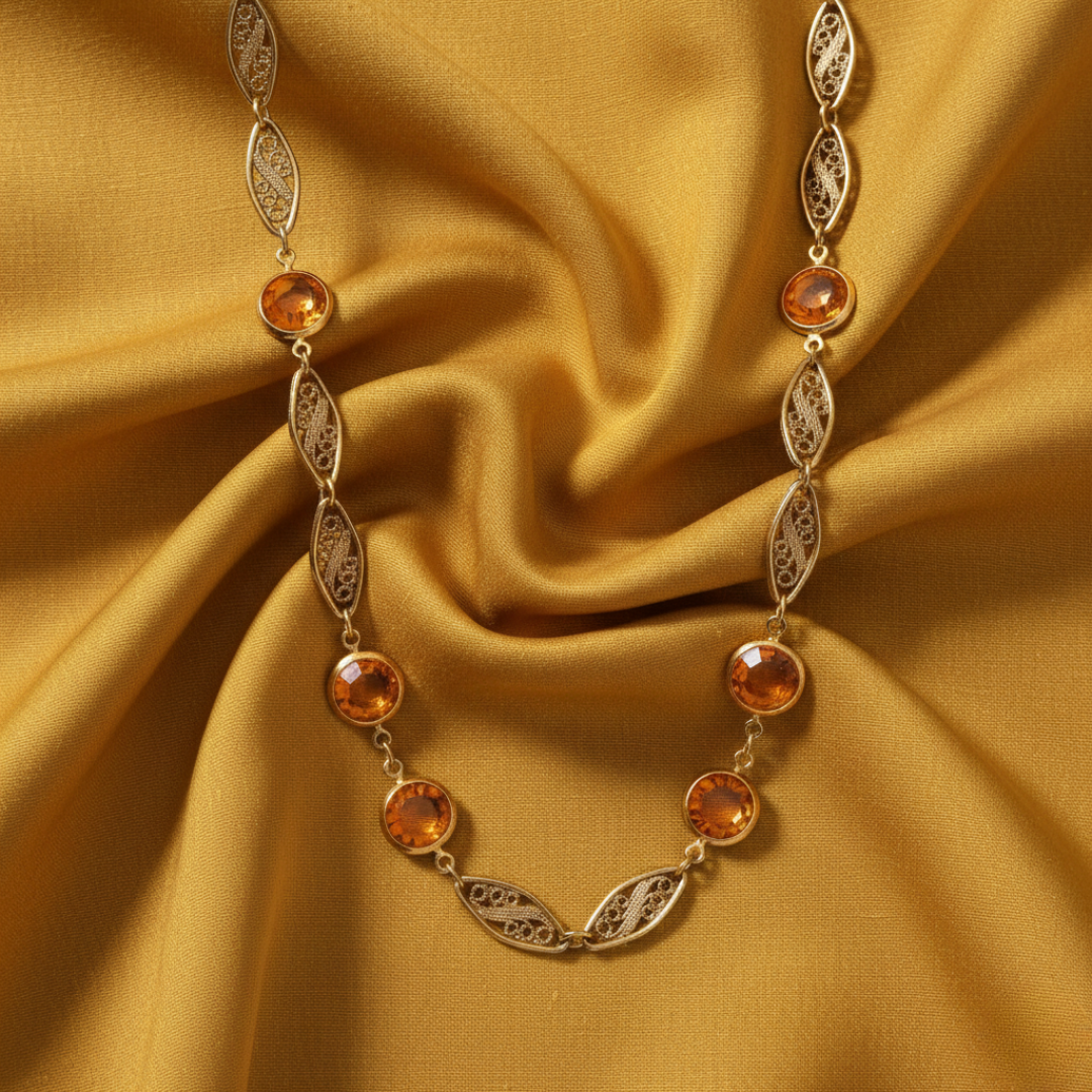 Gold necklace with orange gemstones on a yellow fabric background