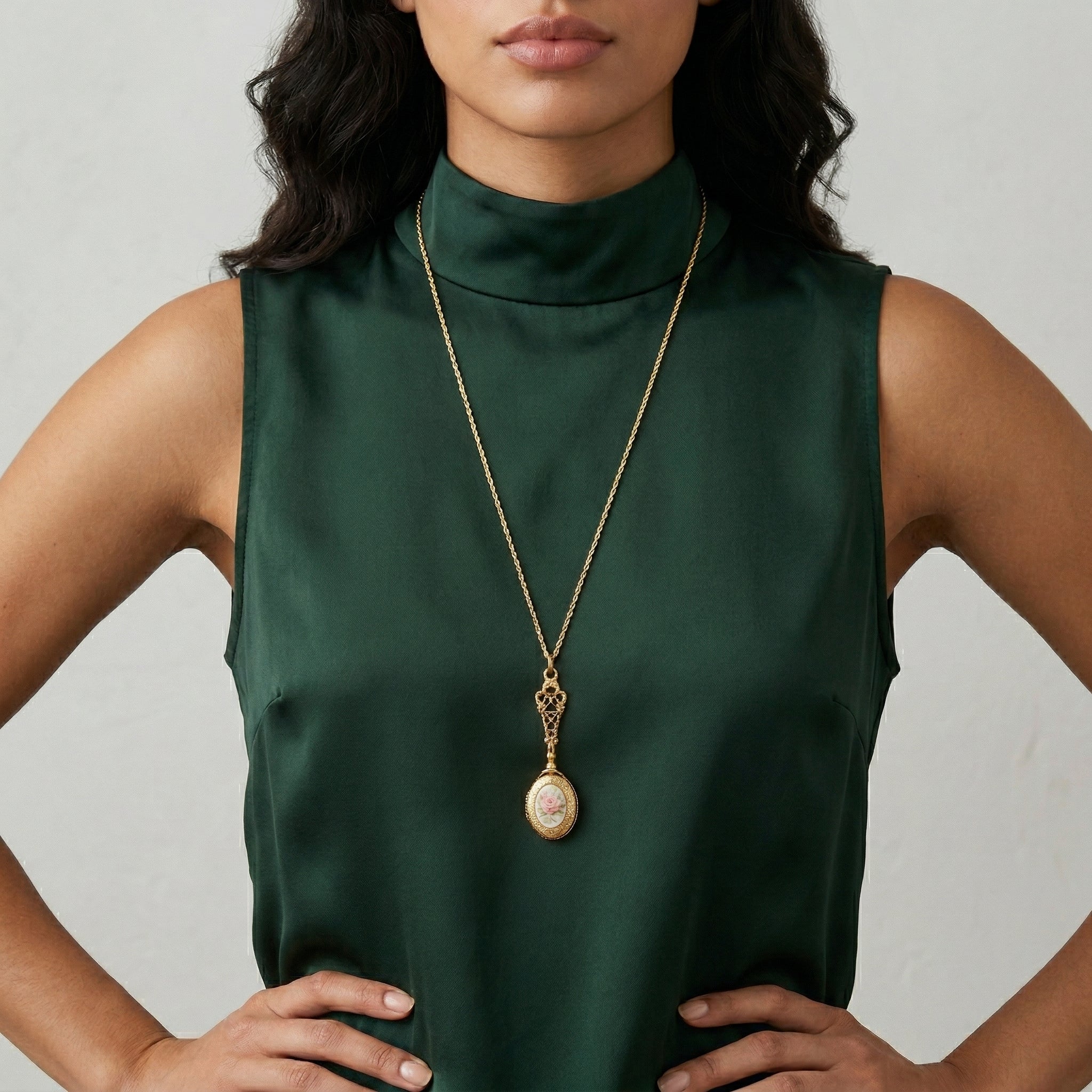 Woman wearing a green sleeveless top and gold locket necklace with a floral pendant.