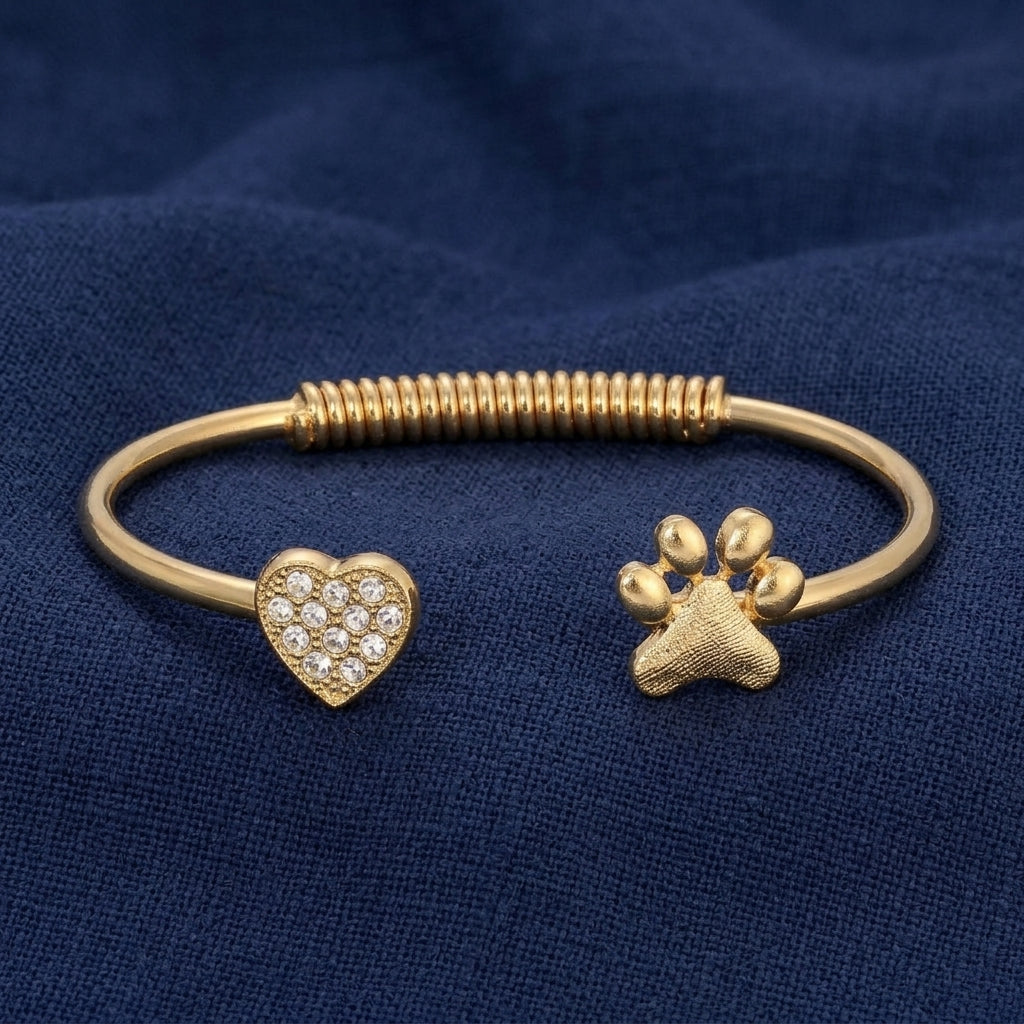 Gold tone heart and pet paw crystal spring bracelet resting on dark navy blue linen surface