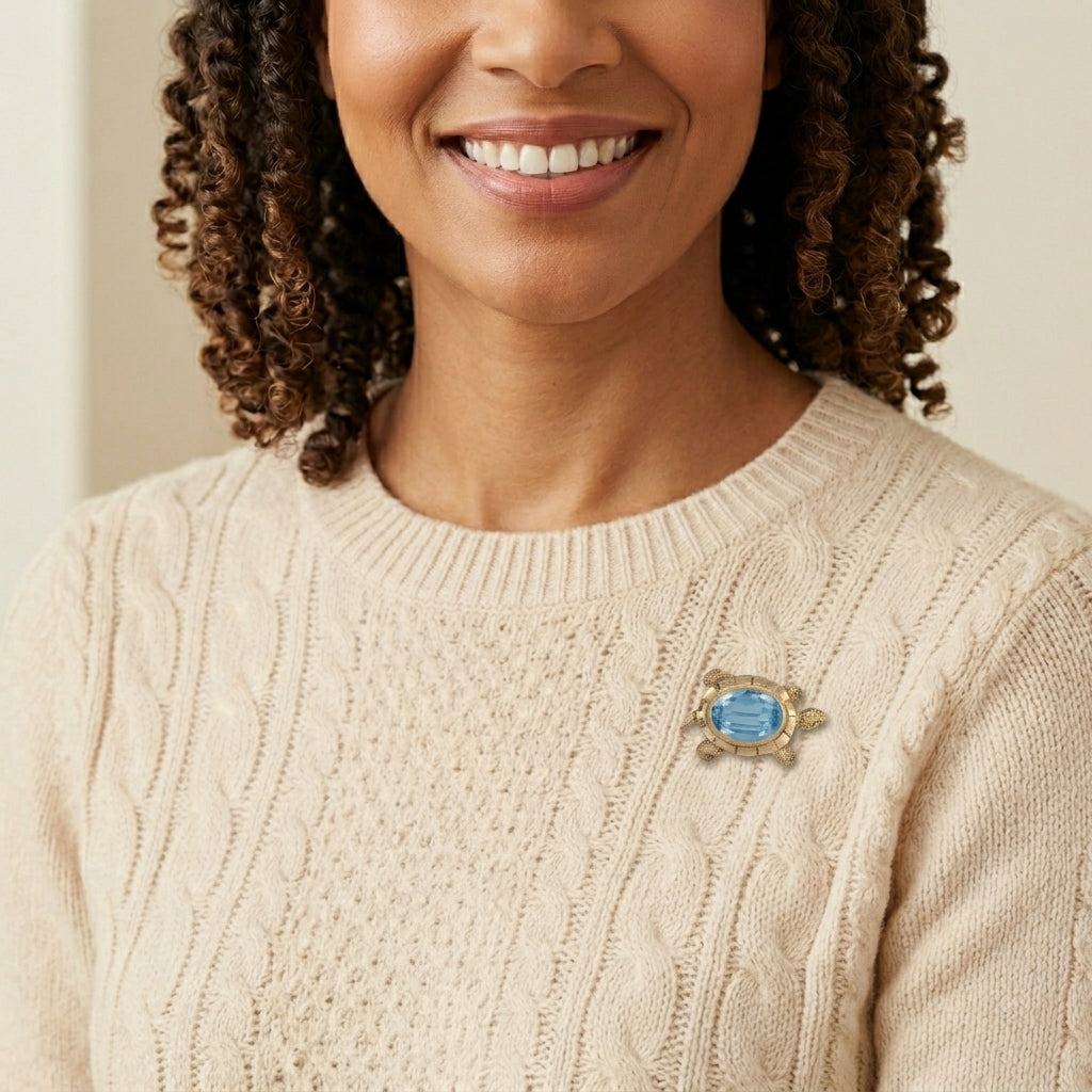 Woman wearing a beige sweater with a decorative tortoise brooch with a blue crystal on a neutral background