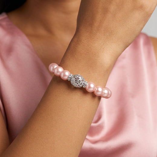 Pink pearl bracelet with silver beads on a wrist against a pink fabric background