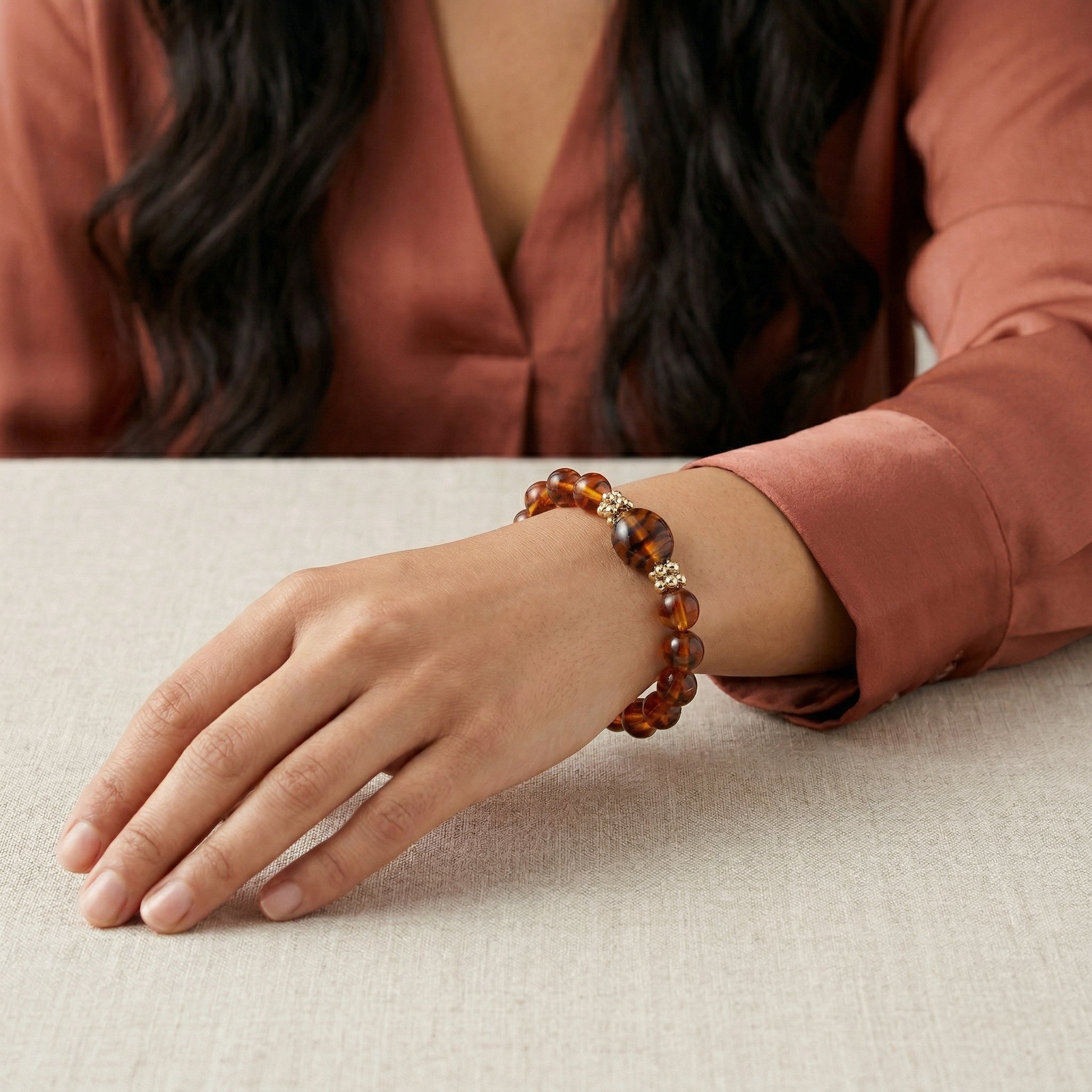 Person wearing a brown beaded bracelet on a neutral background