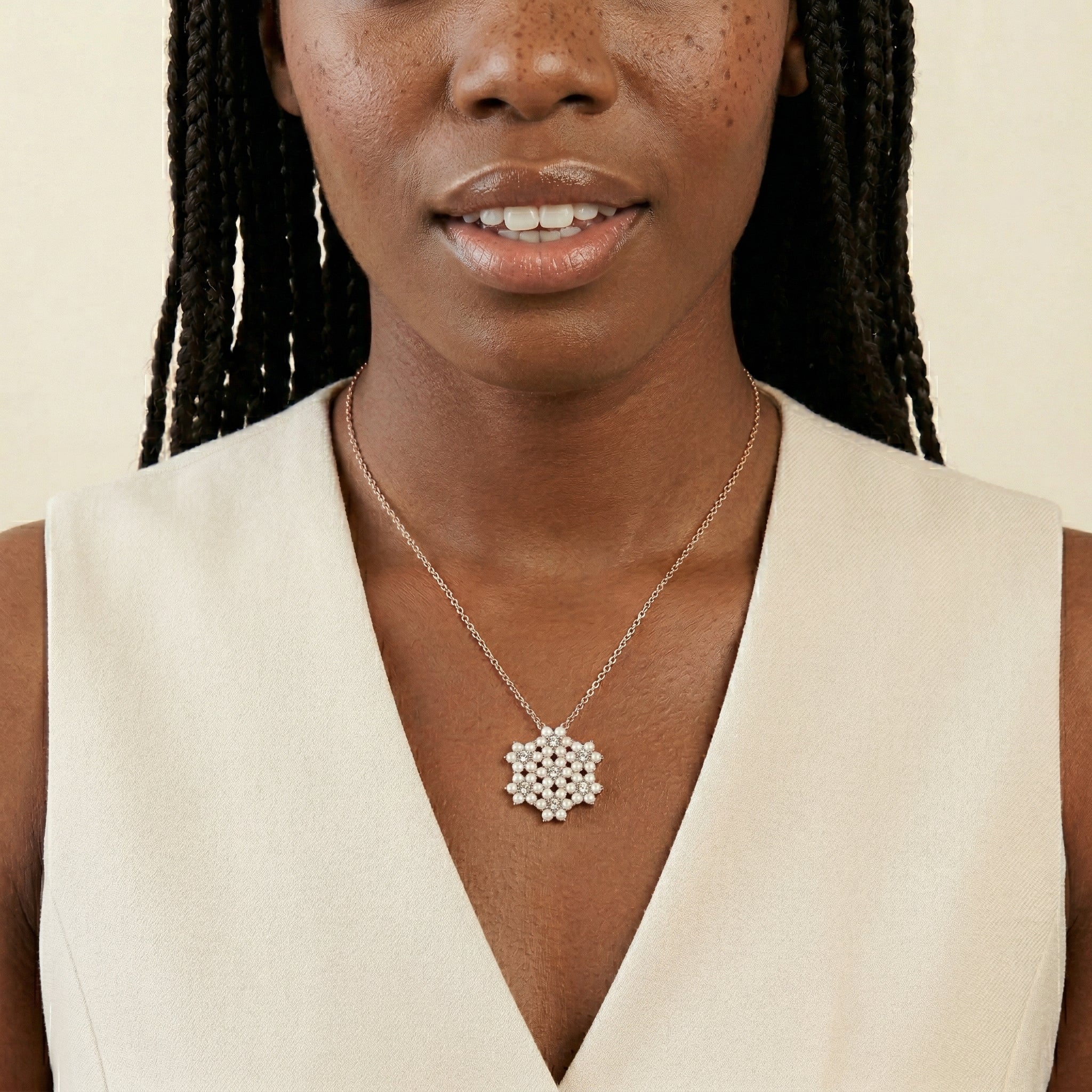 Woman wearing a necklace with a glistening snowflake pendant that has crystals against a beige background