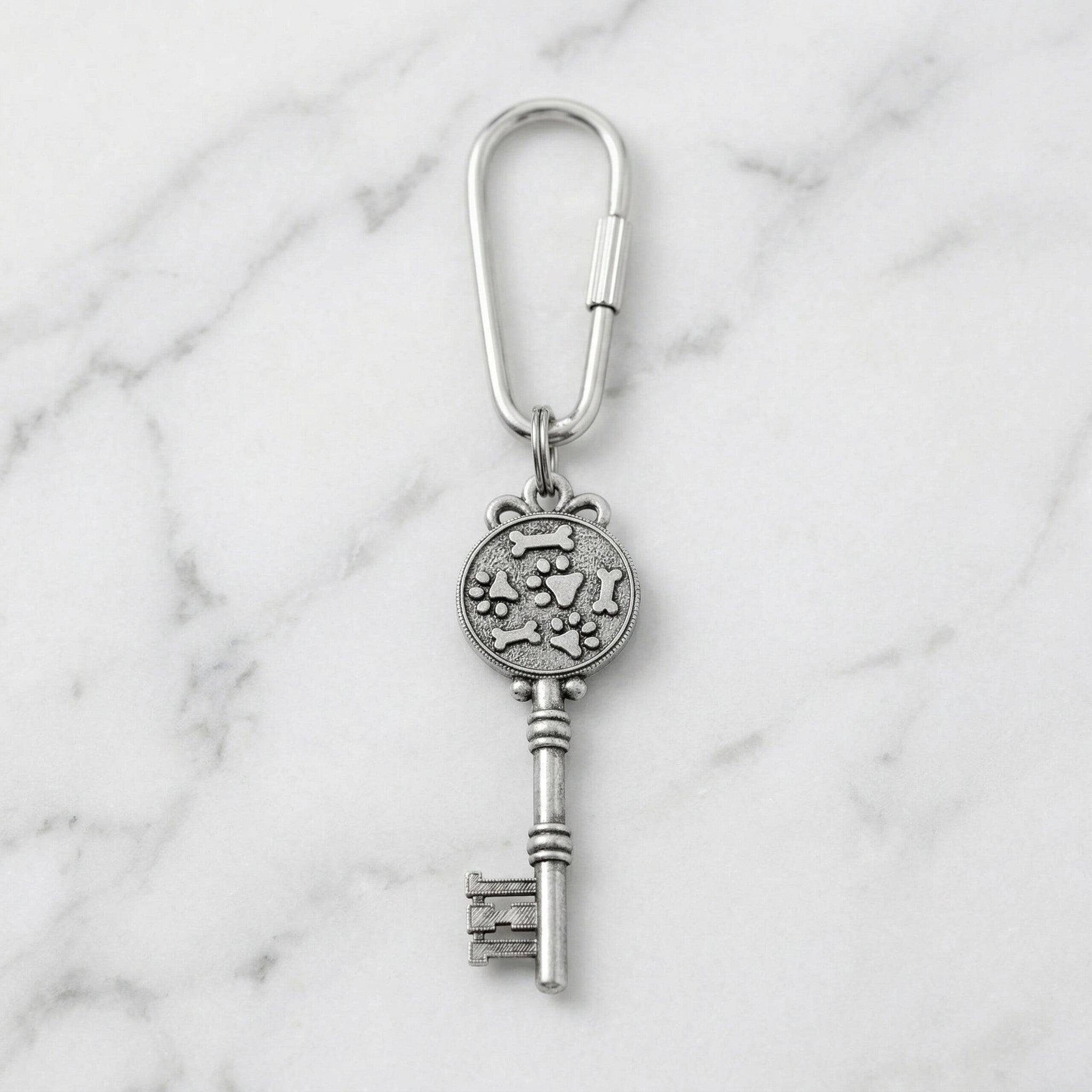 Silver key-shaped keychain with dog paws and bones design on a marble background