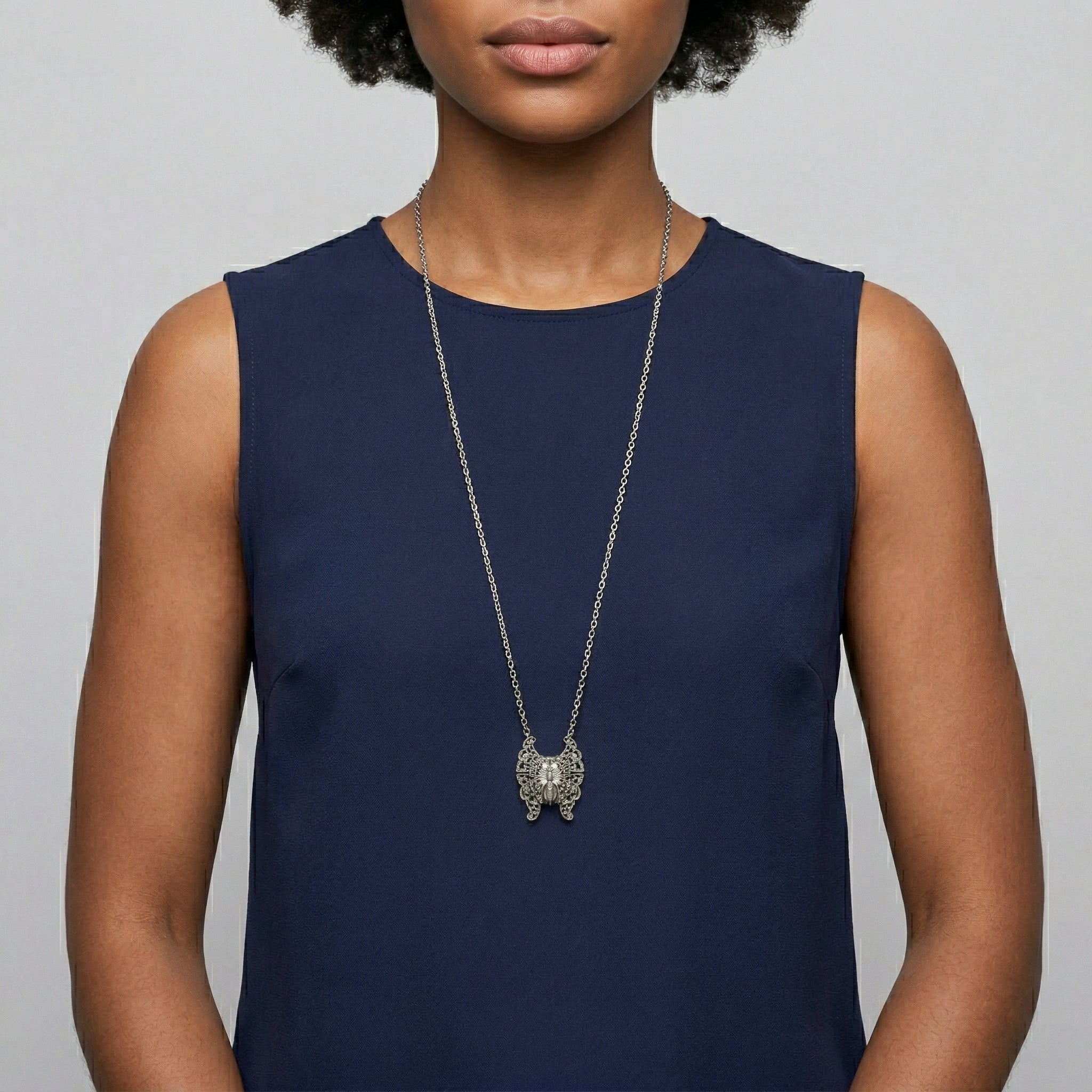 Woman wearing a long necklace with a butterfly locket pendant on a plain background