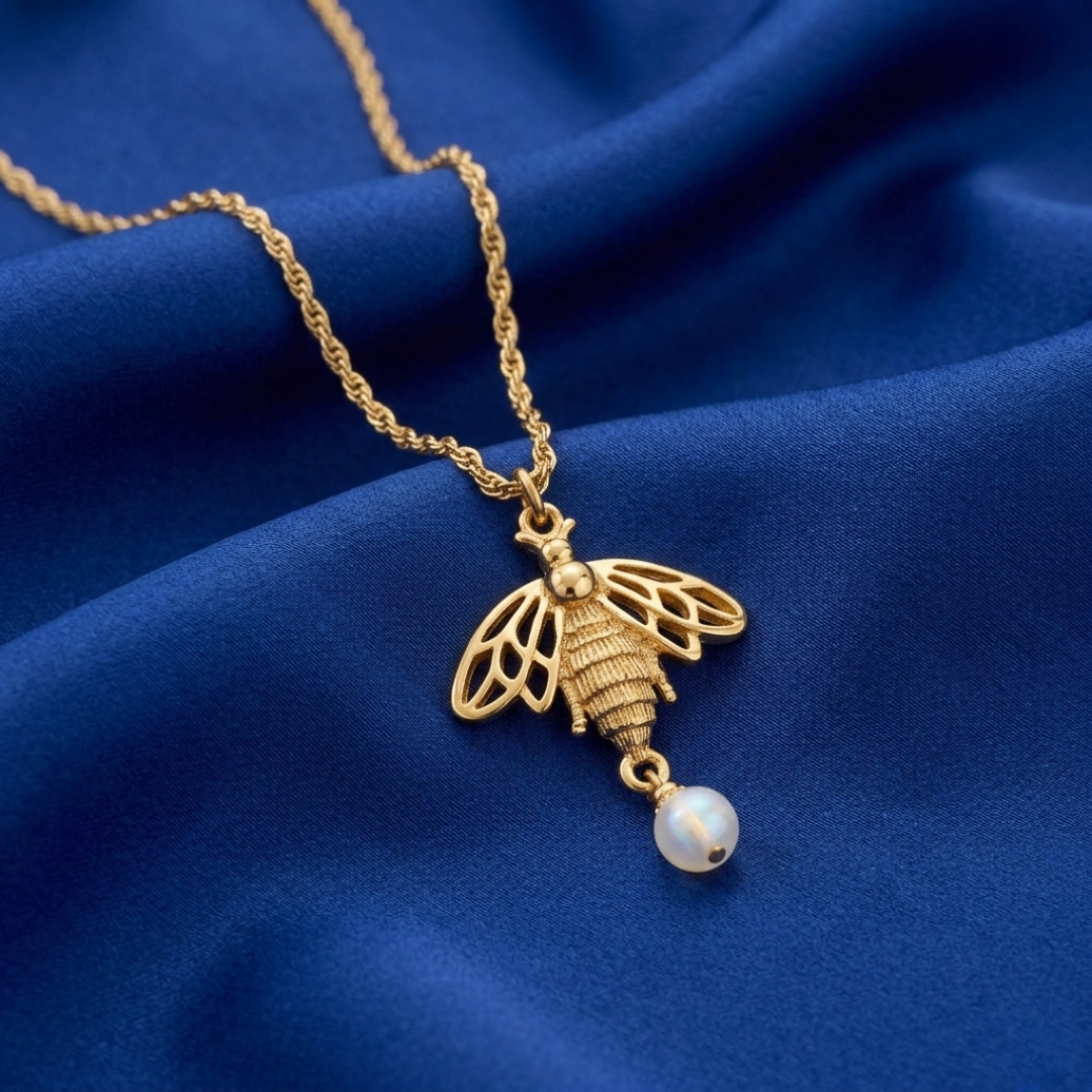 Gold necklace with a bee pendant and pearl on a blue fabric background