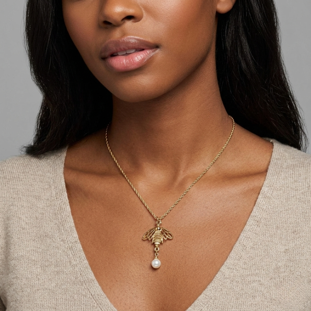 Woman wearing a gold necklace with a bee pendant and pearl drop against a gray background
