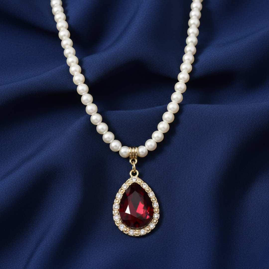 Faux pearl necklace with a red teardrop pendant linked with crystals on a blue fabric background
