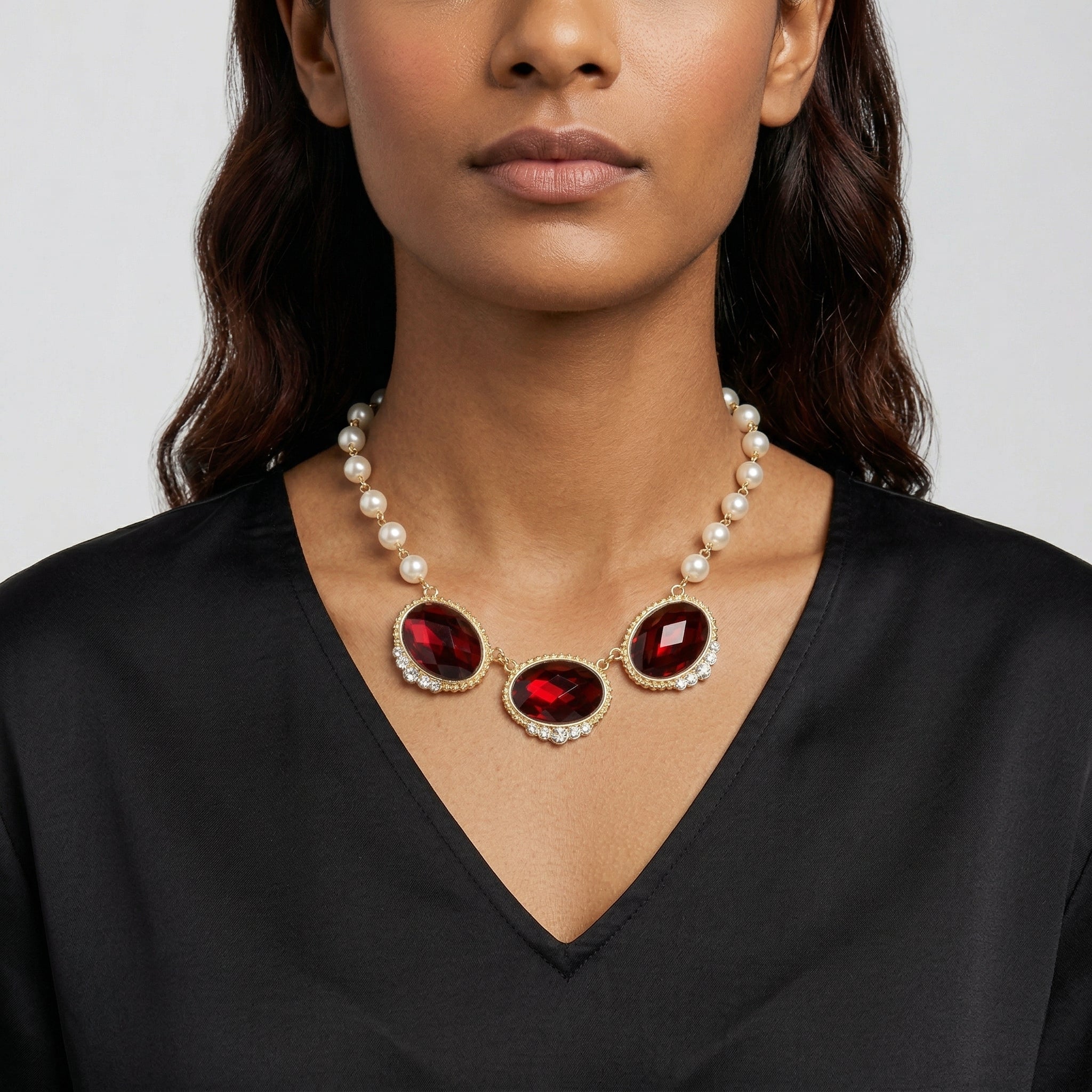 Woman wearing a pearl necklace with large siam red crystals on a plain background