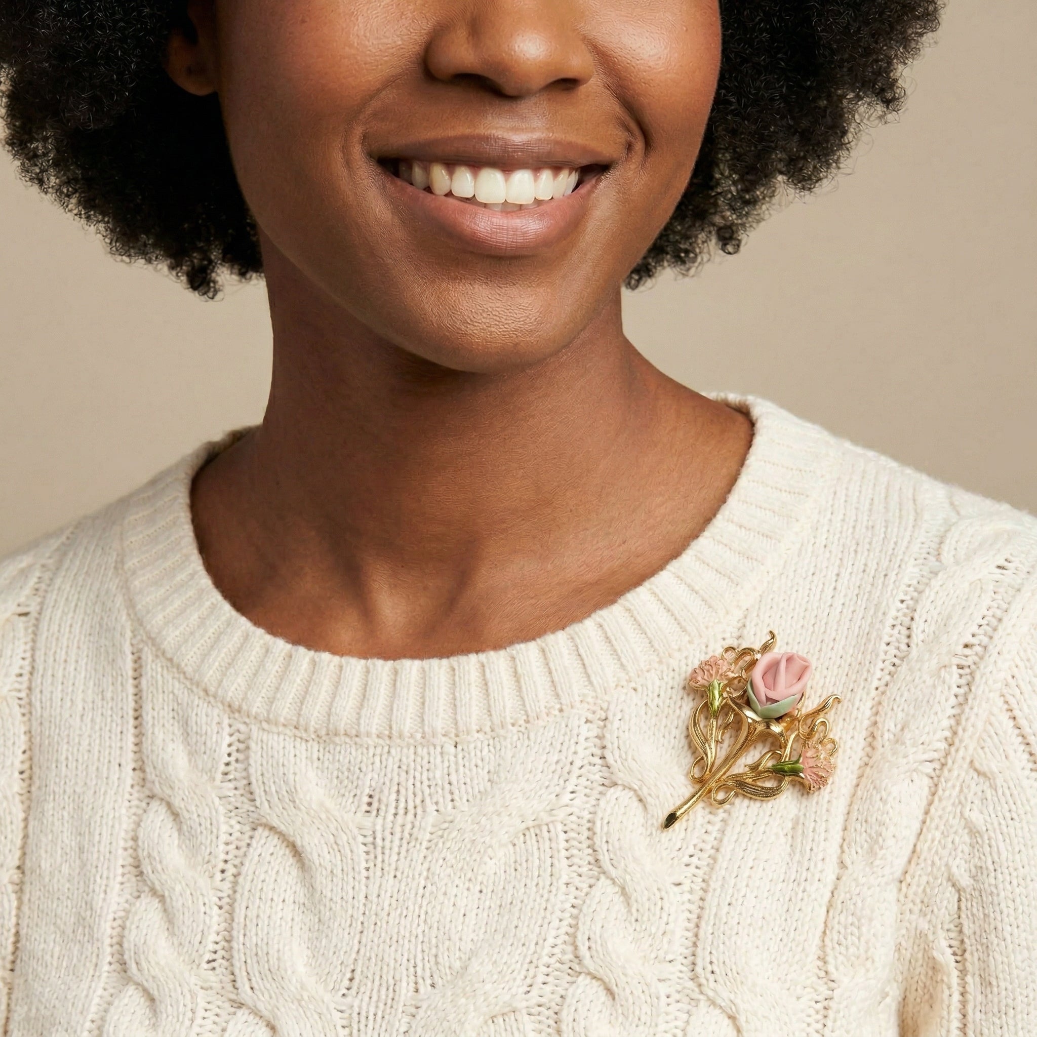 Woman wearing a cream sweater with a floral porcelain rose brooch on a beige background