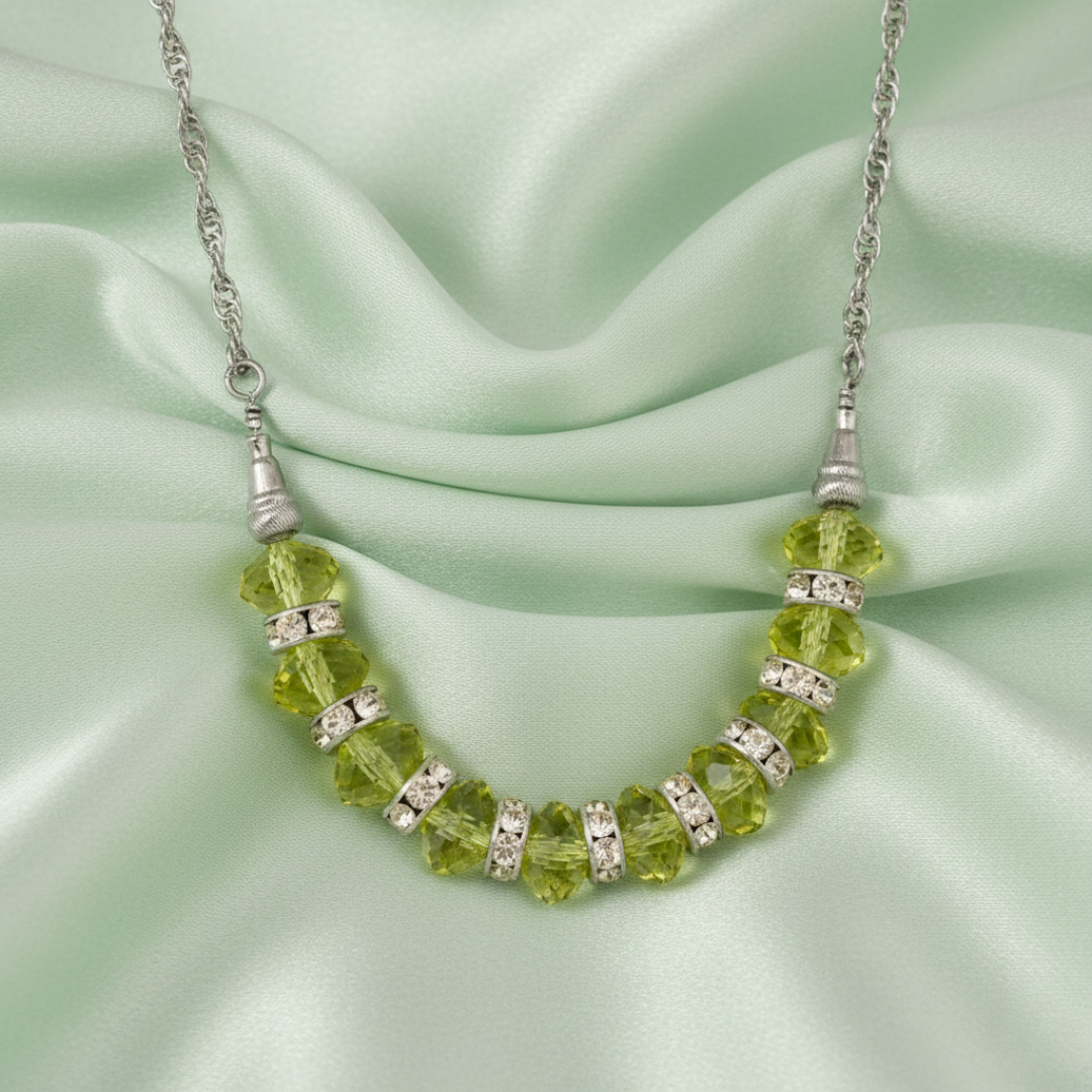 Necklace with green beads and silver accents on a light green fabric background