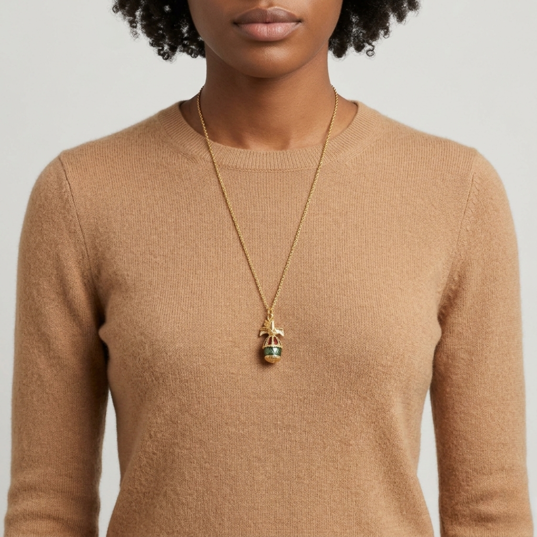 Person wearing a gold necklace with a dove bird and egg pendant on a plain background