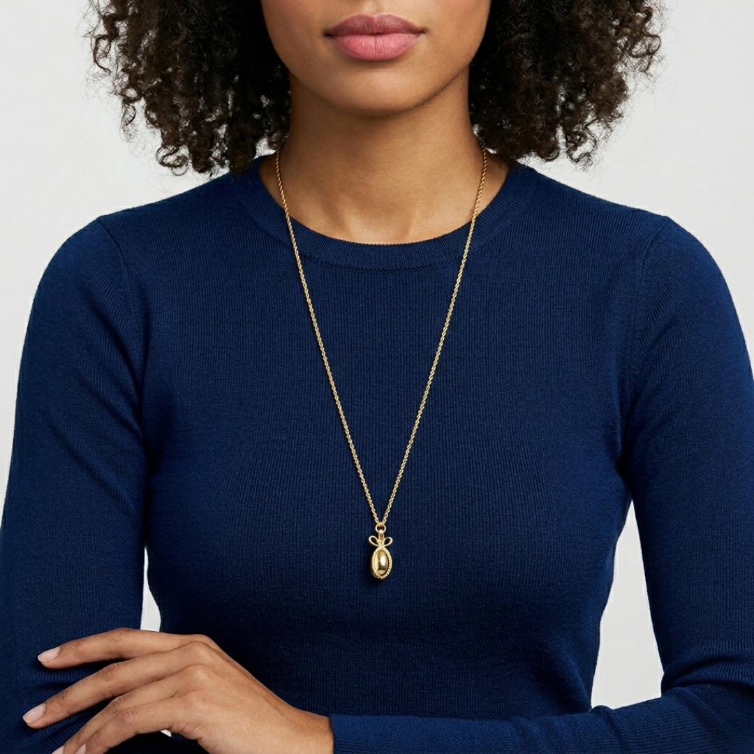 Woman wearing a golden egg pendant necklace with a blue top against a neutral background